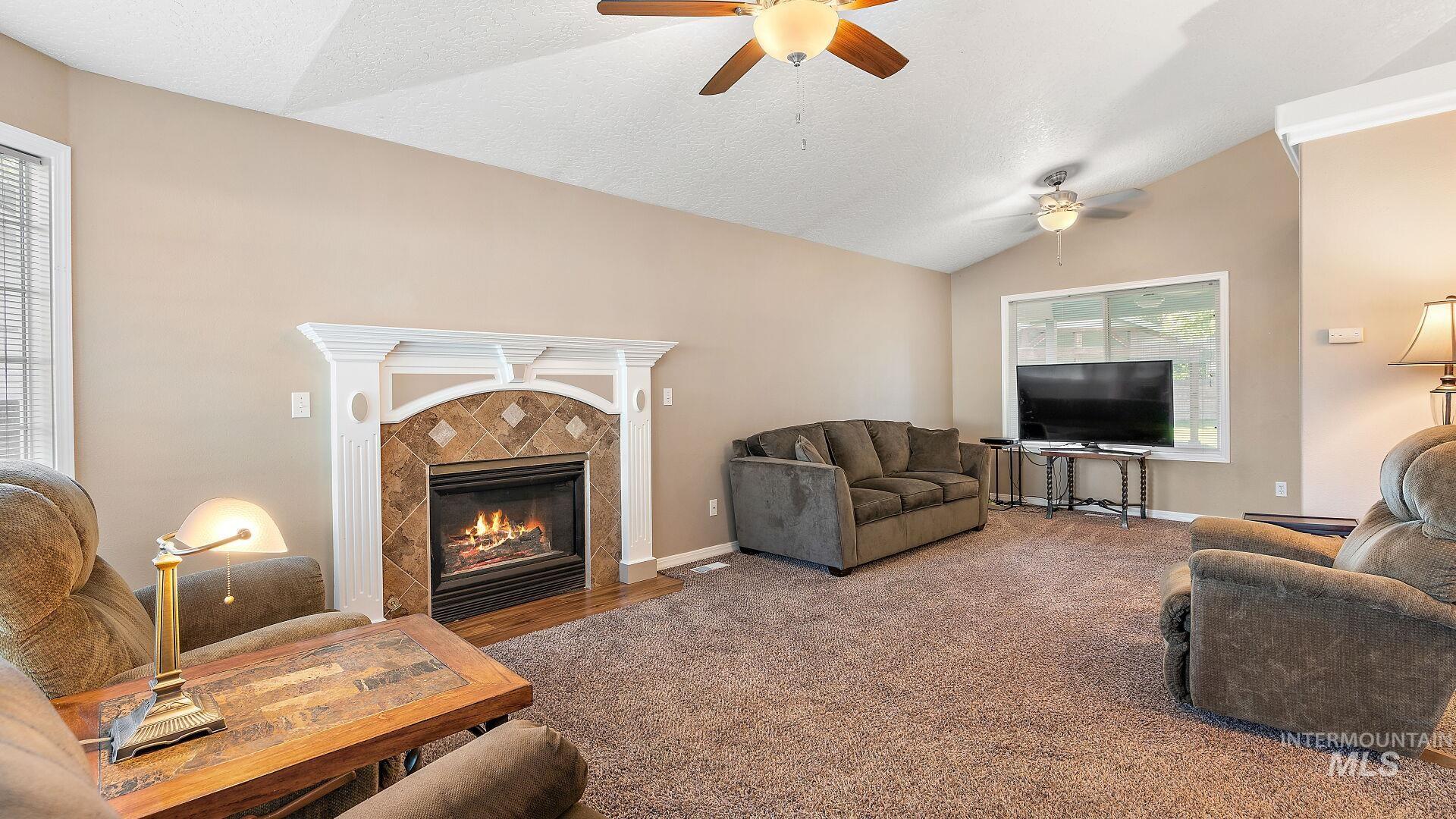 Living area featuring lofted ceiling, carpet flooring, a fireplace, a textured ceiling, and a ceiling fan