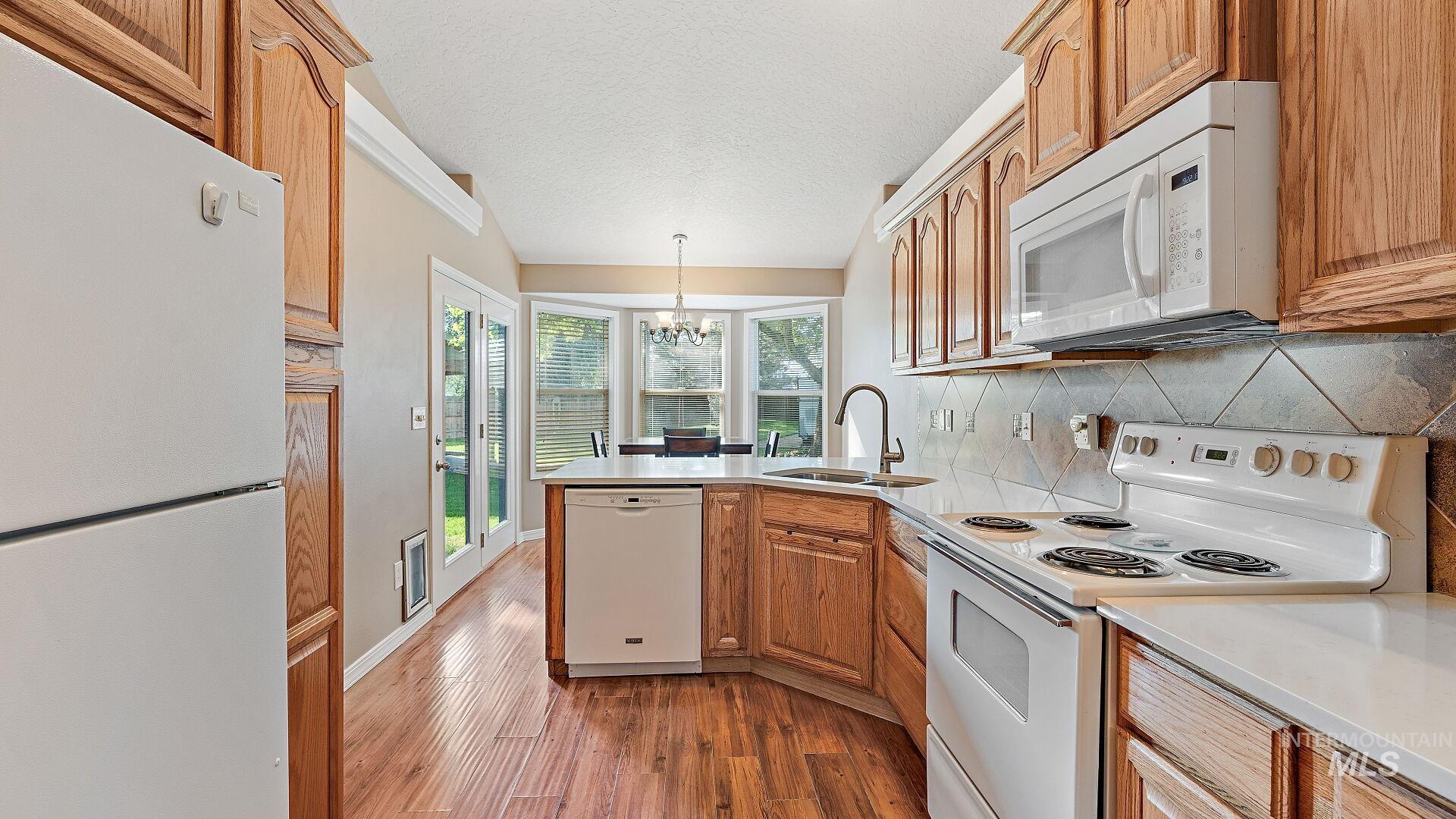 Kitchen with white appliances, a peninsula, a chandelier, brown cabinetry, and dark wood finished floors