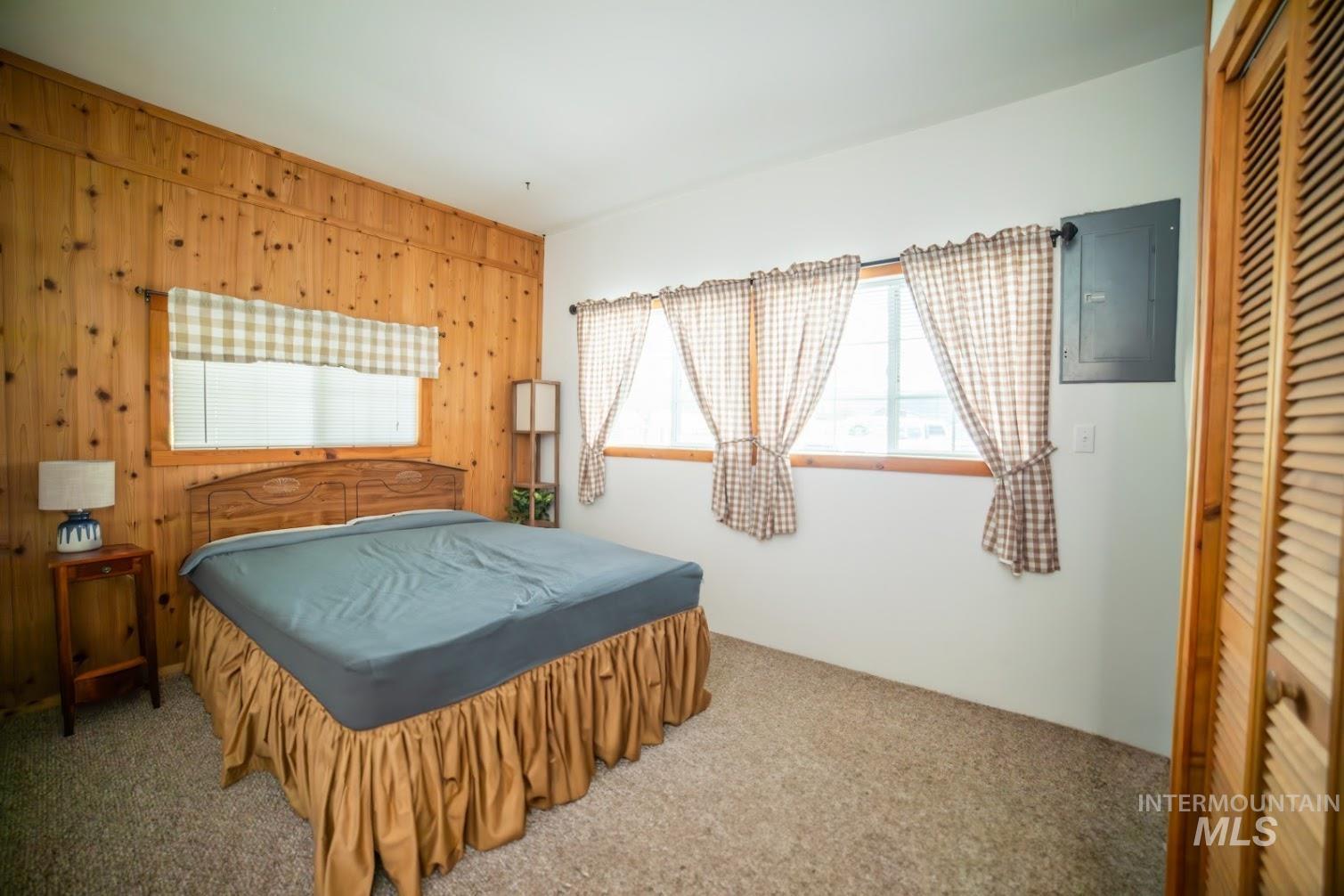 Bedroom with wood walls, carpet flooring, electric panel, and a closet