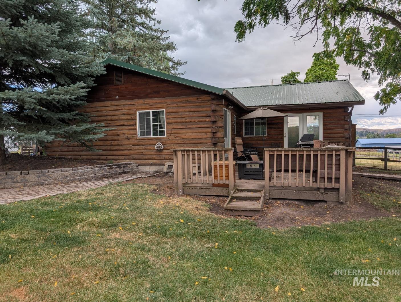 Back of property featuring log exterior, a wooden deck, a yard, and a metal roof