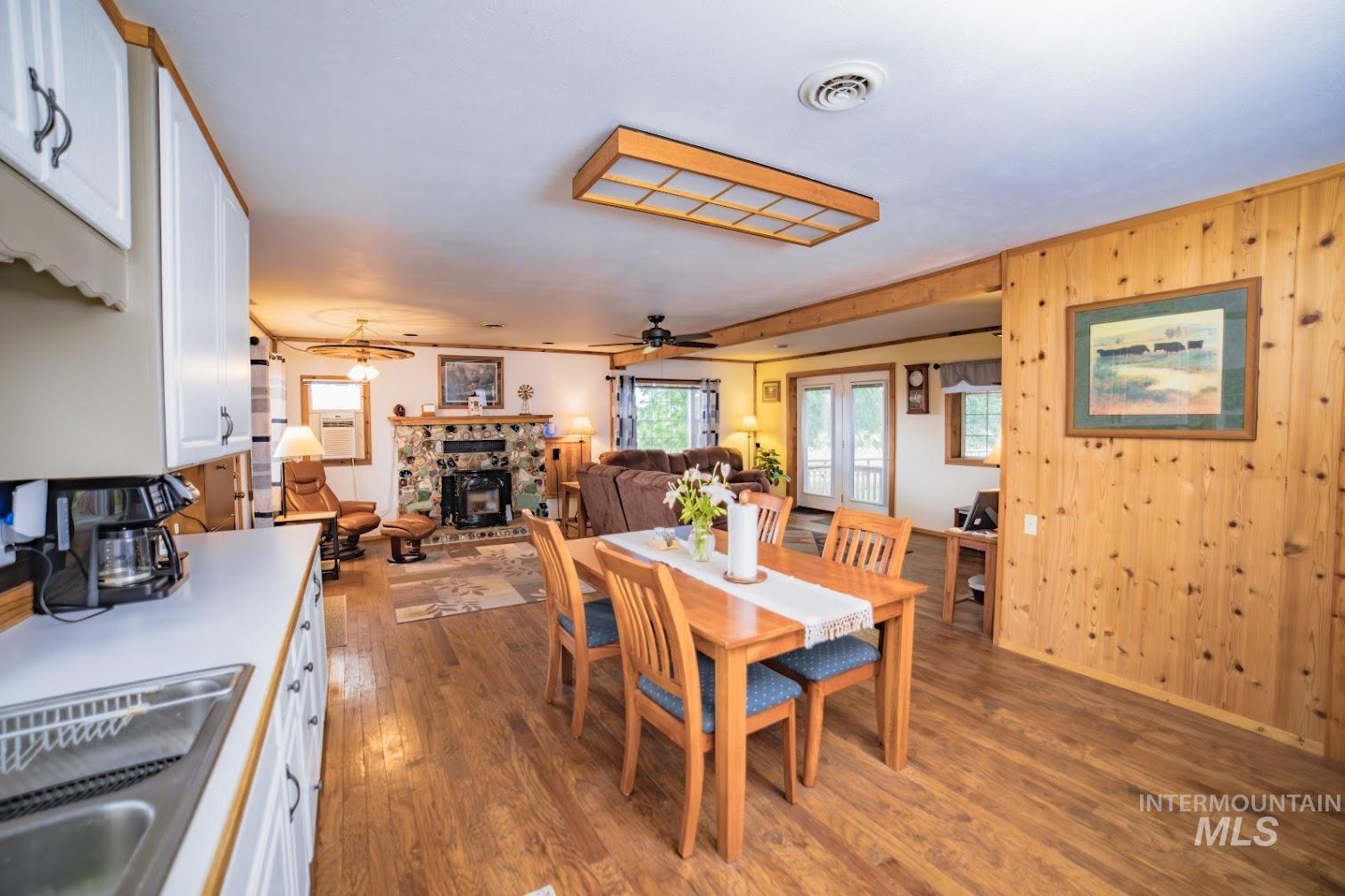 Dining area featuring dark wood-type flooring, wooden walls, ceiling fan, and a fireplace with raised hearth