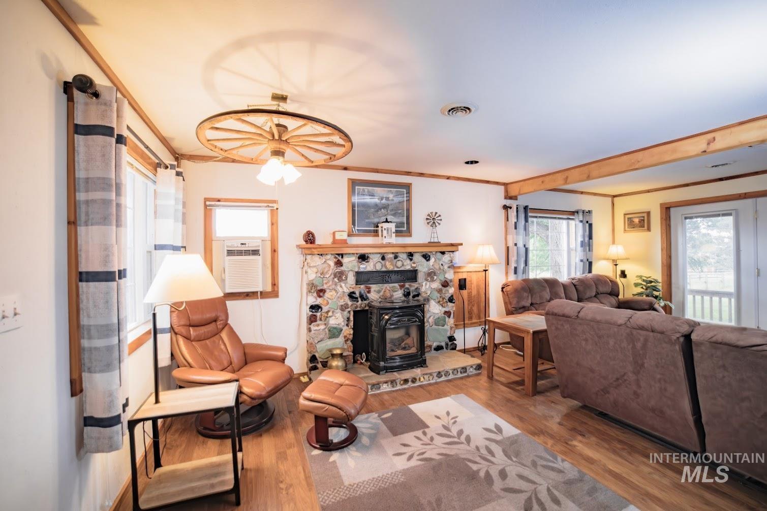 Living area with crown molding, wood finished floors, a wood stove, and beamed ceiling