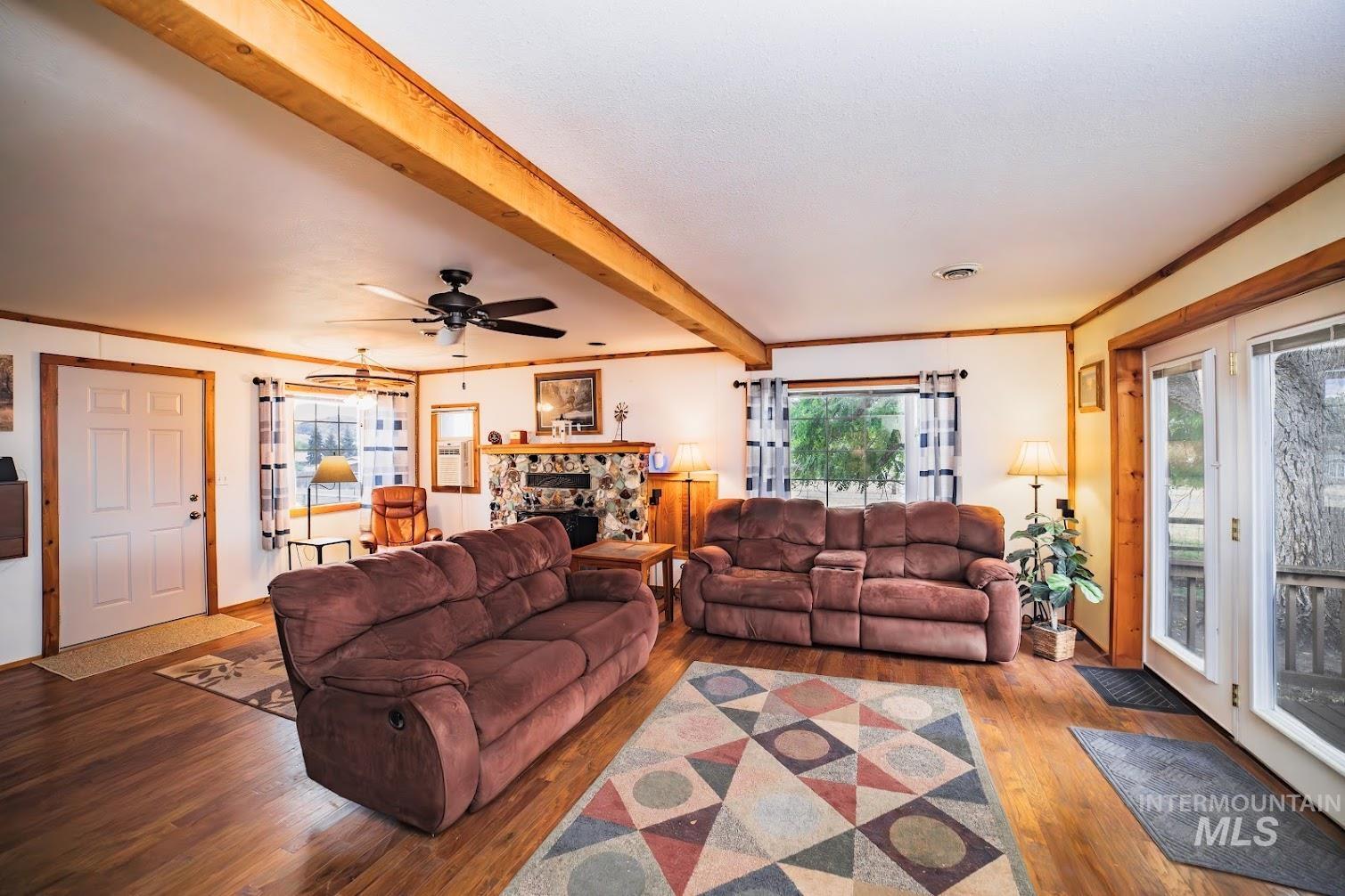 Living area with wood finished floors, ornamental molding, beamed ceiling, a fireplace, and a ceiling fan