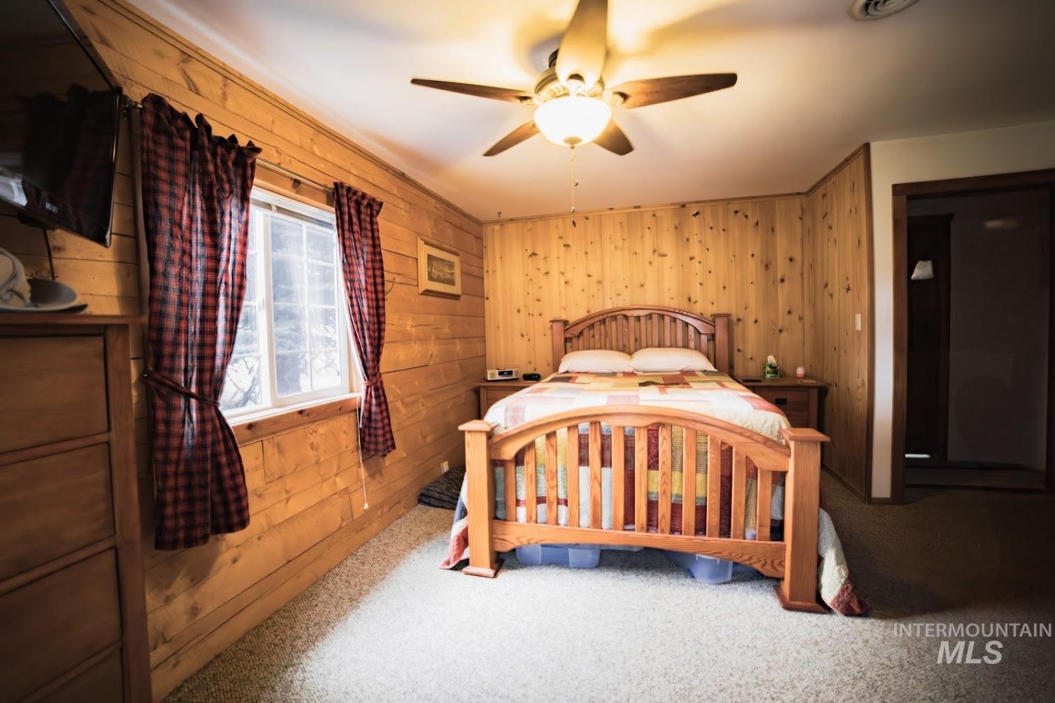 Carpeted bedroom with wood walls and ceiling fan