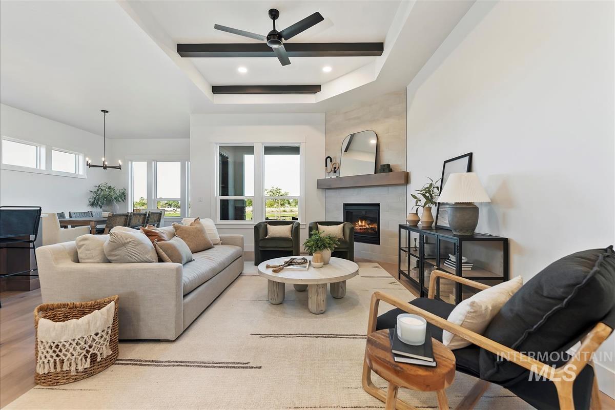 Living room with a tray ceiling, a fireplace, a ceiling fan, light wood finished floors, and a chandelier