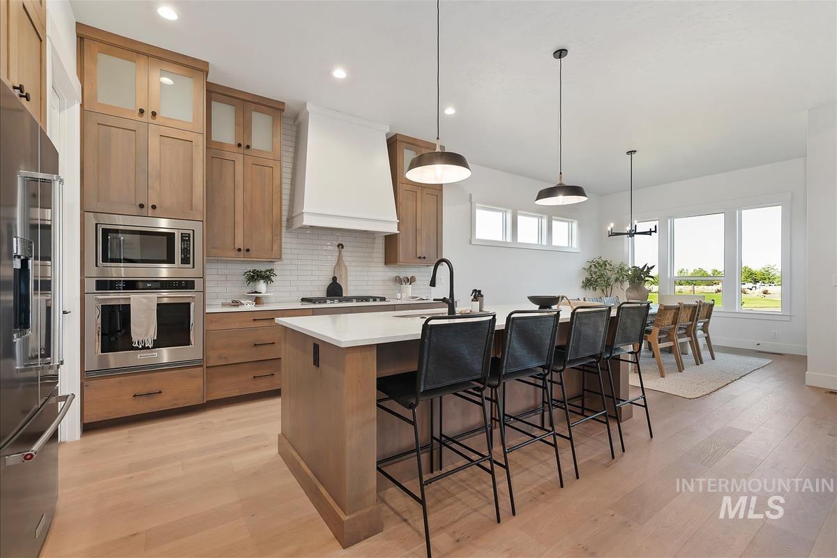 Kitchen with pendant lighting, backsplash, appliances with stainless steel finishes, a kitchen bar, and light wood finished floors