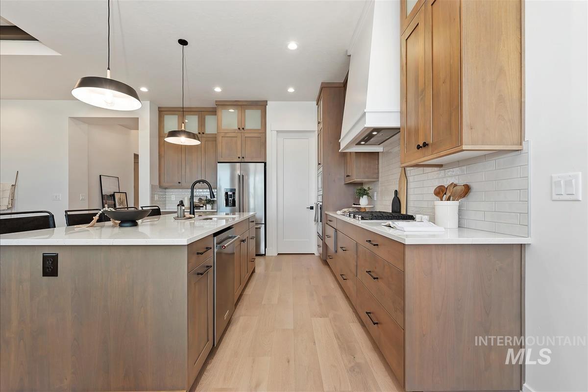 Kitchen with a large island with sink, glass insert cabinets, hanging light fixtures, a breakfast bar, and backsplash