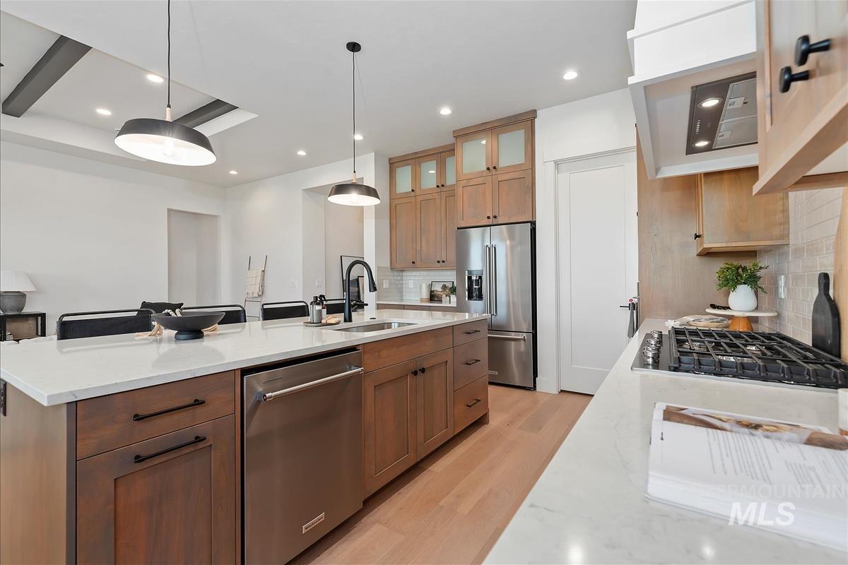 Kitchen with light stone countertops, appliances with stainless steel finishes, light wood-type flooring, decorative light fixtures, and recessed lighting