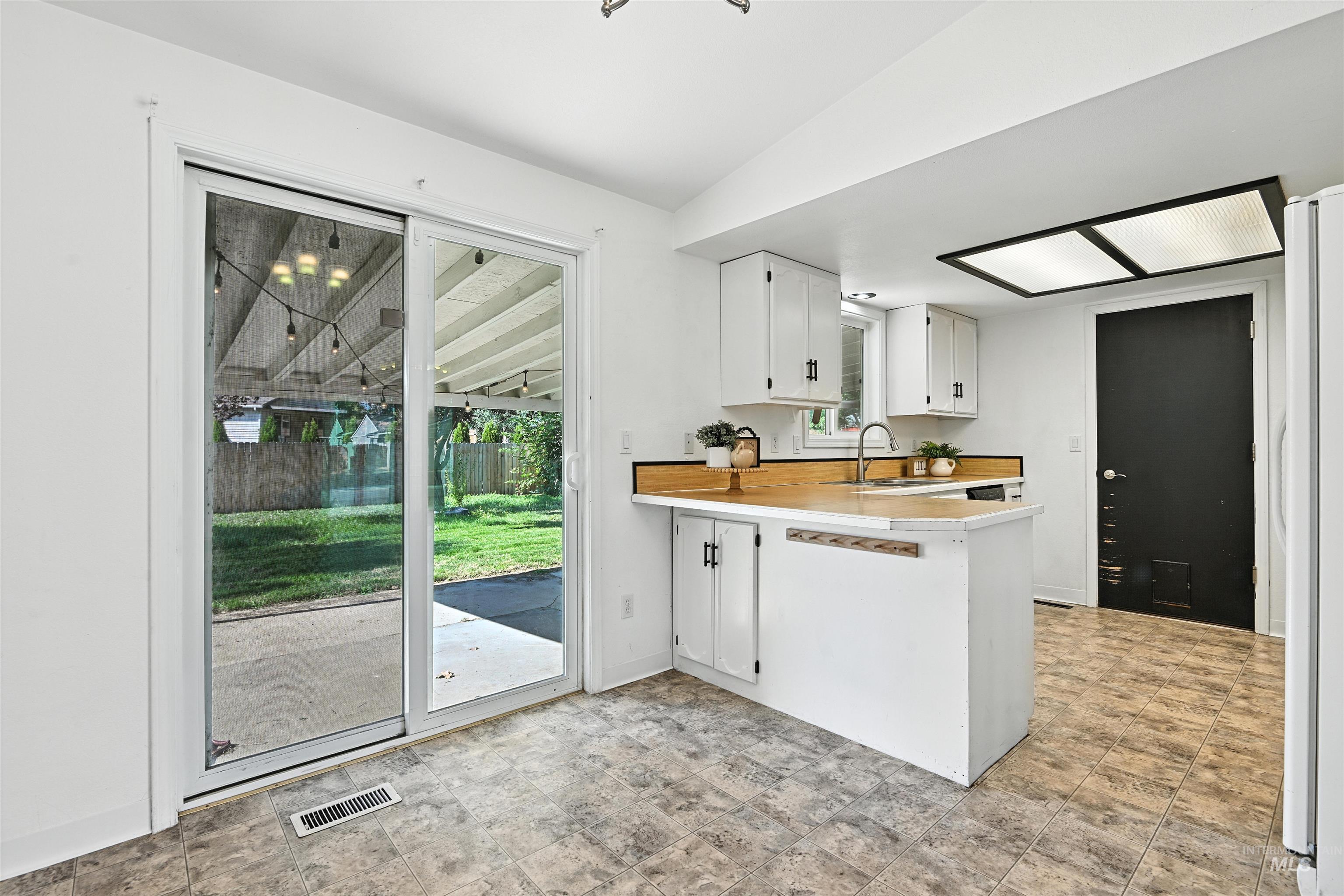 Kitchen featuring light countertops, a peninsula, freestanding refrigerator, and white cabinetry