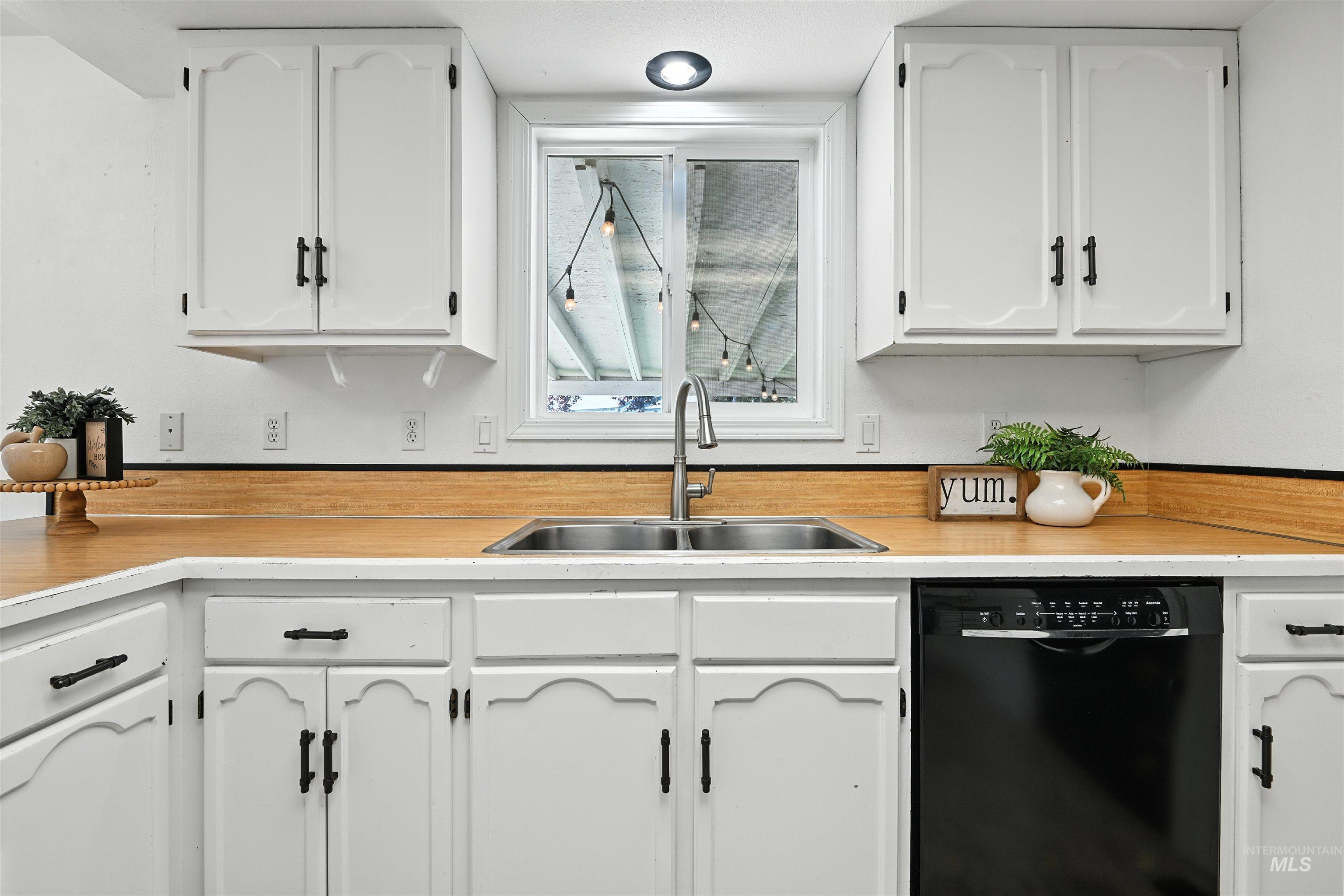 Kitchen with black dishwasher, white cabinetry, and light countertops