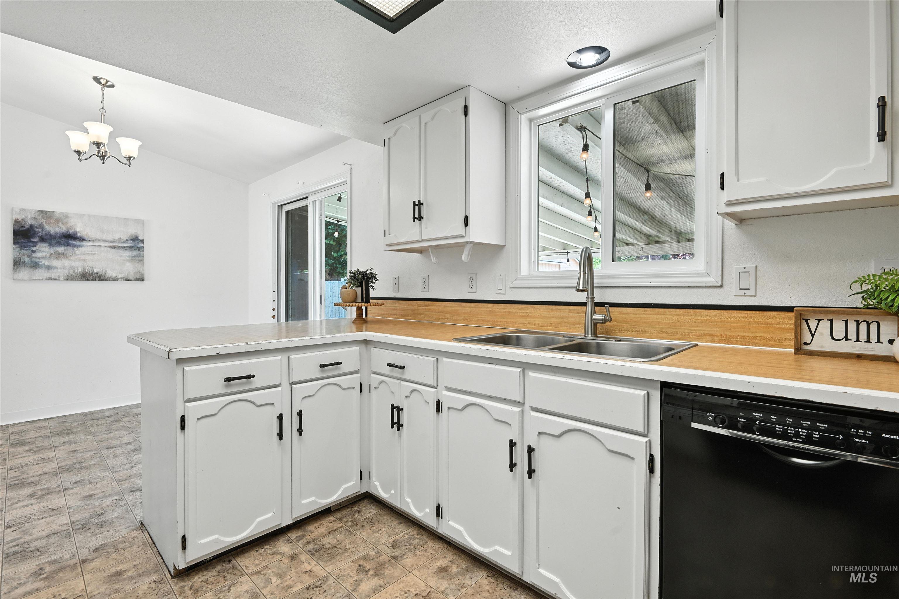 Kitchen with black dishwasher, a peninsula, vaulted ceiling, white cabinets, and light countertops