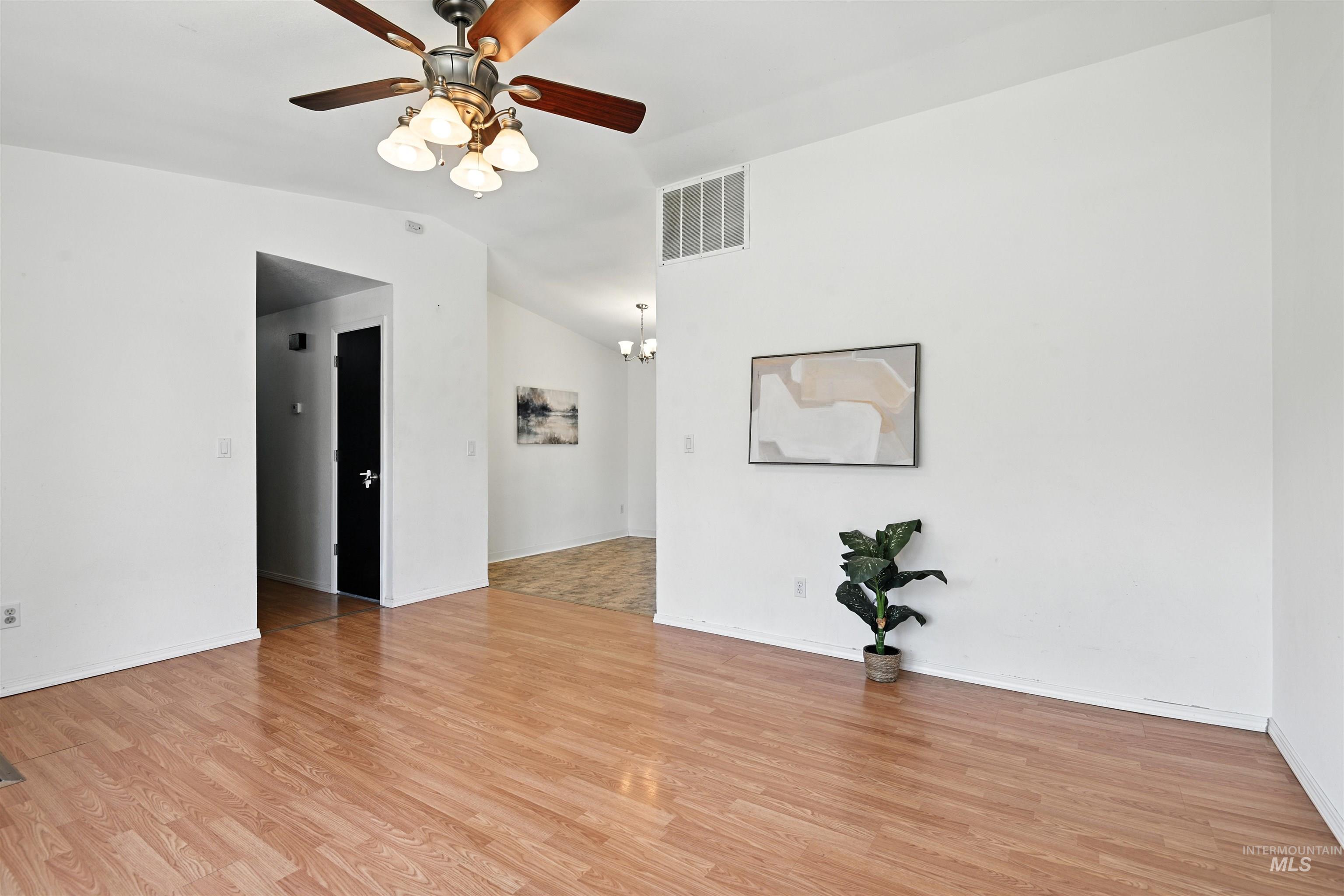 Empty room with ceiling fan, light wood finished floors, a chandelier, and lofted ceiling