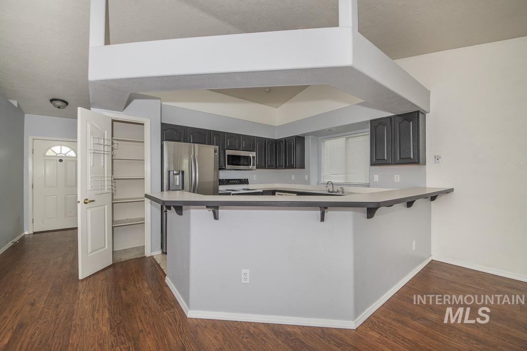 Kitchen featuring a breakfast bar area, stainless steel appliances, dark wood-style floors, and light countertops