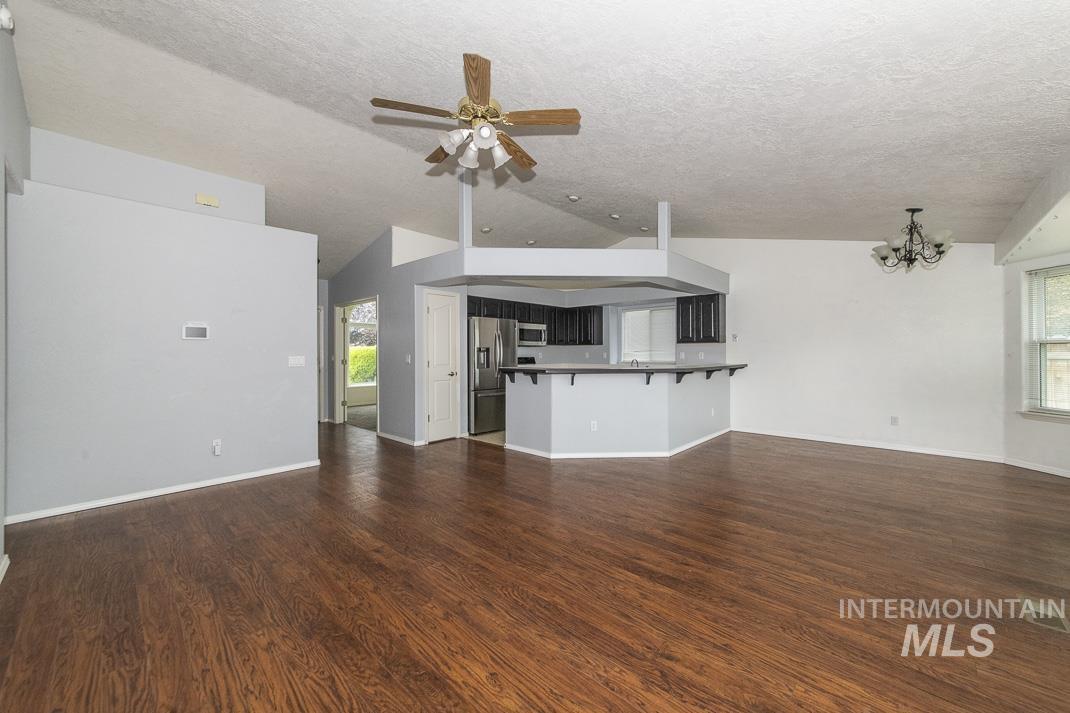 Unfurnished living room with dark wood-style flooring, a textured ceiling, vaulted ceiling, a ceiling fan, and a chandelier