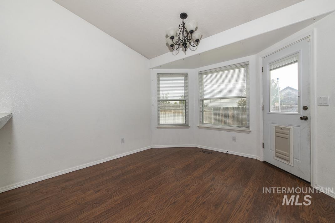 Unfurnished dining area with dark wood-style flooring, lofted ceiling, and a chandelier