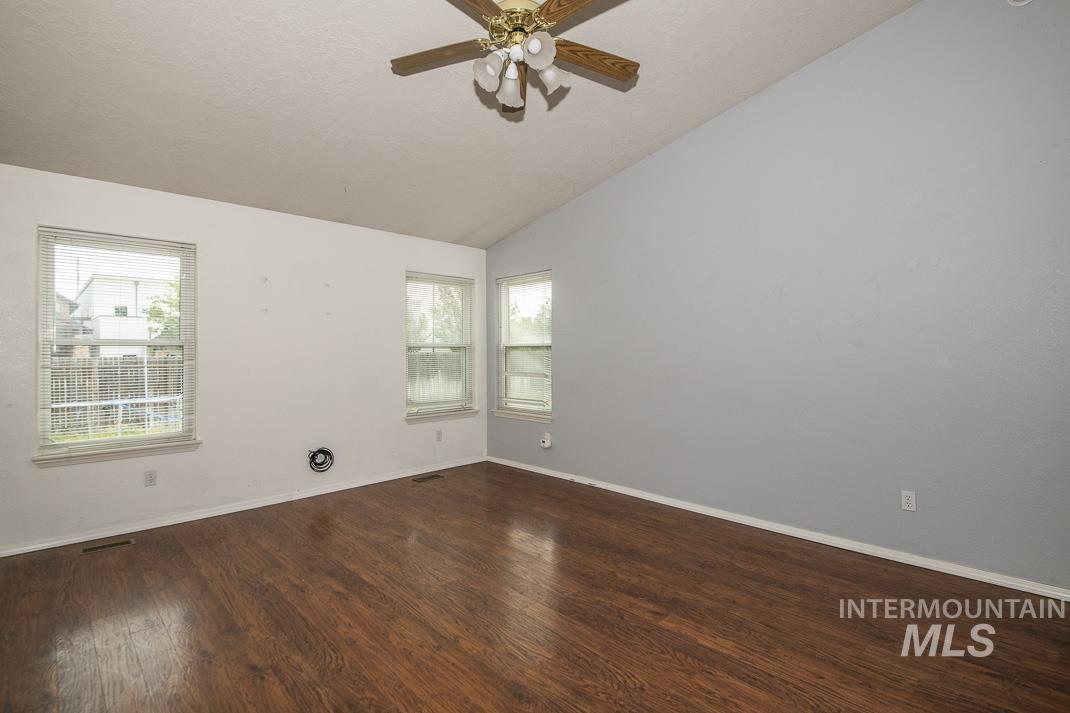 Empty room with lofted ceiling, dark wood-type flooring, and ceiling fan