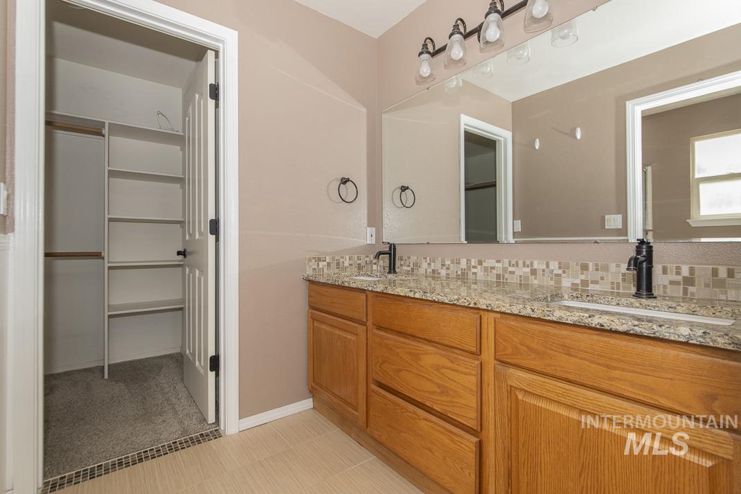 Full bath with double vanity, a spacious closet, and decorative backsplash
