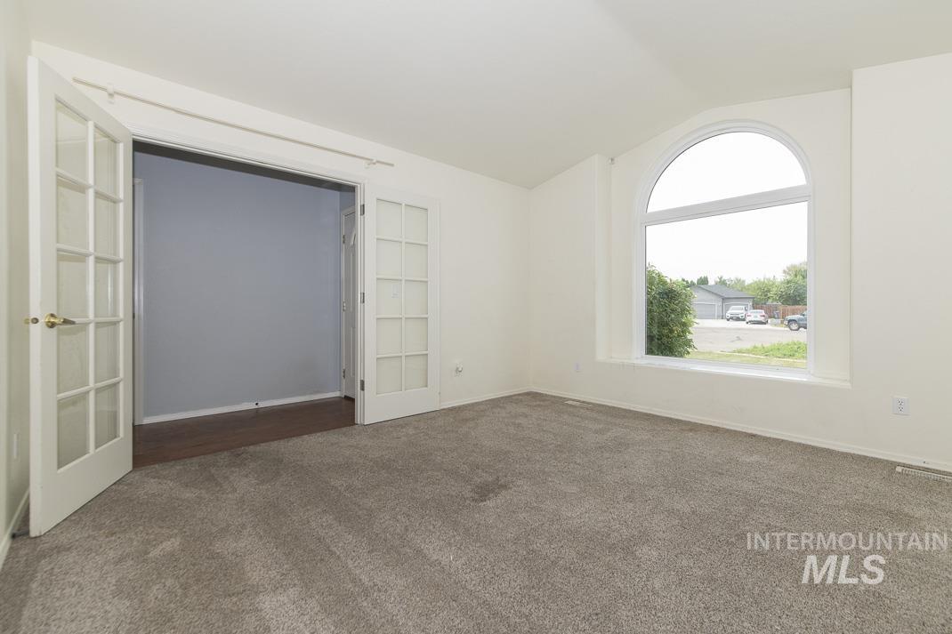 Unfurnished room featuring lofted ceiling, dark colored carpet, and french doors