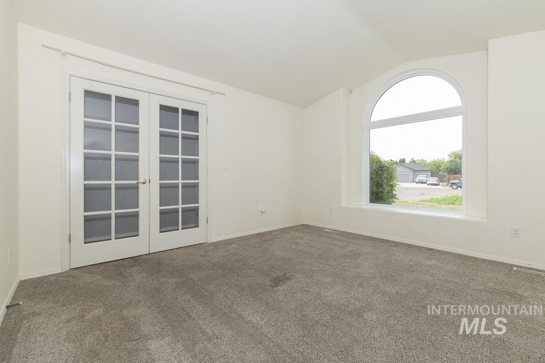 Carpeted spare room with french doors and vaulted ceiling