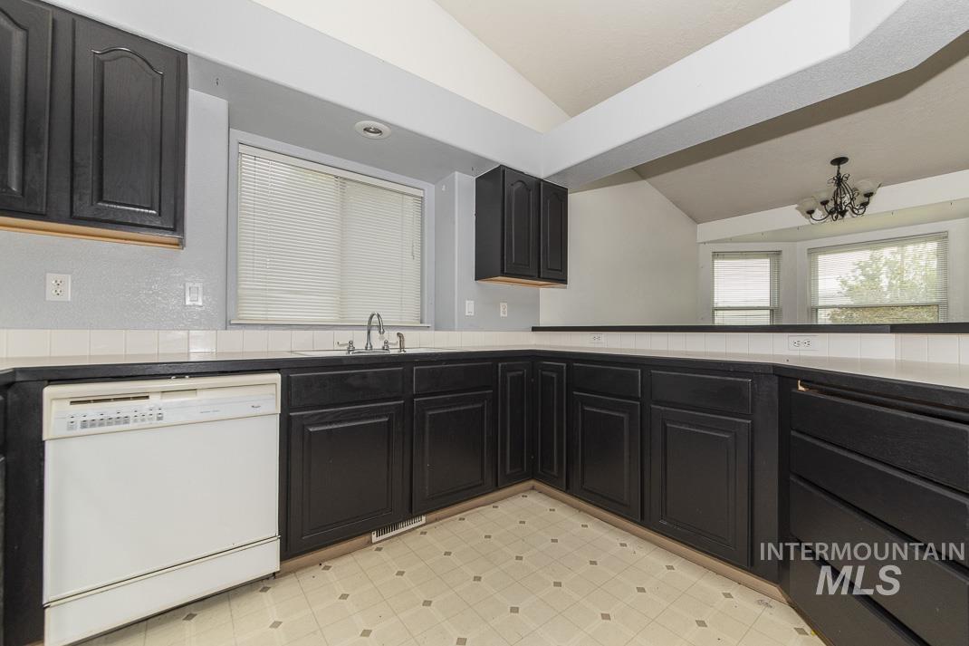Kitchen featuring dark cabinetry, dishwasher, light flooring, lofted ceiling, and a chandelier