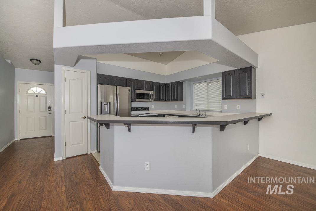 Kitchen with a kitchen breakfast bar, stainless steel appliances, and dark wood-type flooring