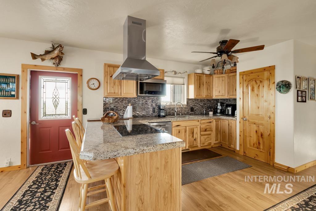 Kitchen featuring a kitchen breakfast bar, light wood-style flooring, tasteful backsplash, and island exhaust hood
