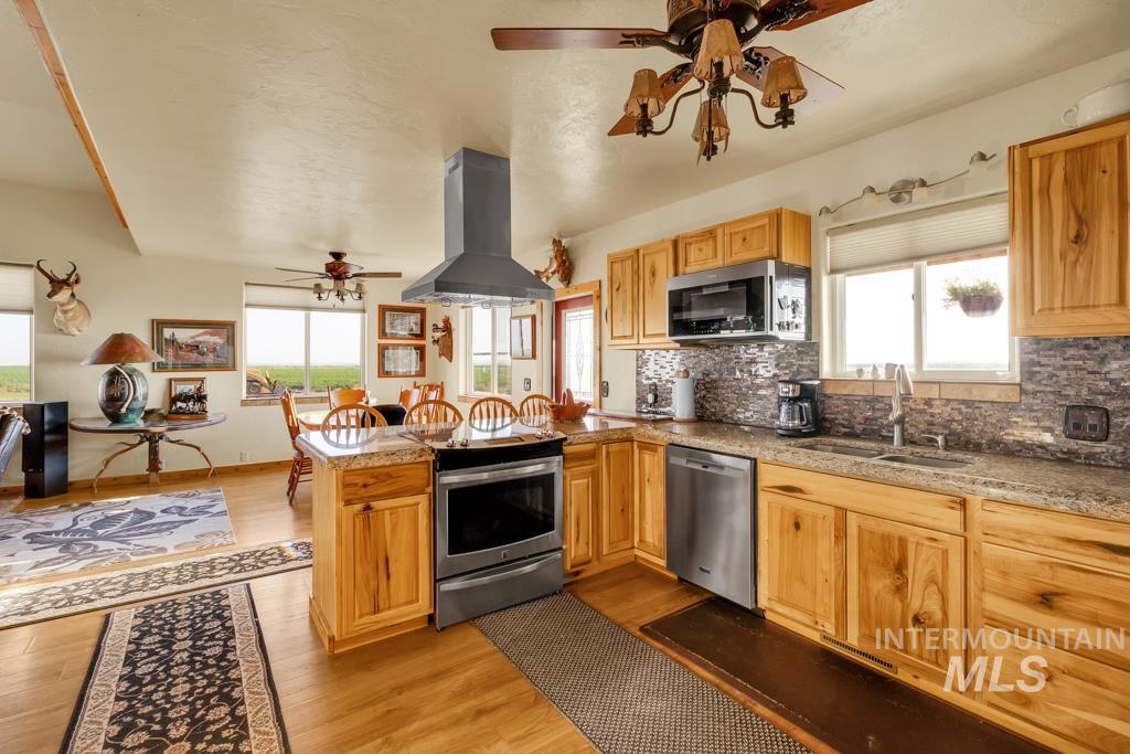 Kitchen with ceiling fan, island range hood, light wood-type flooring, and plenty of natural light