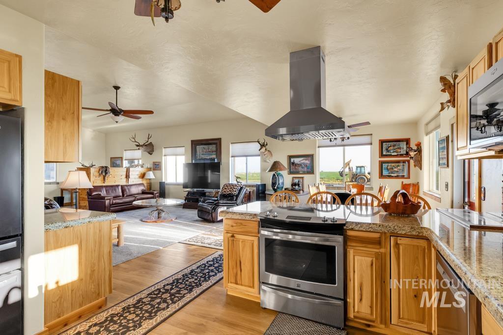 Kitchen with light stone counters, stainless steel appliances, island range hood, and light wood-type flooring