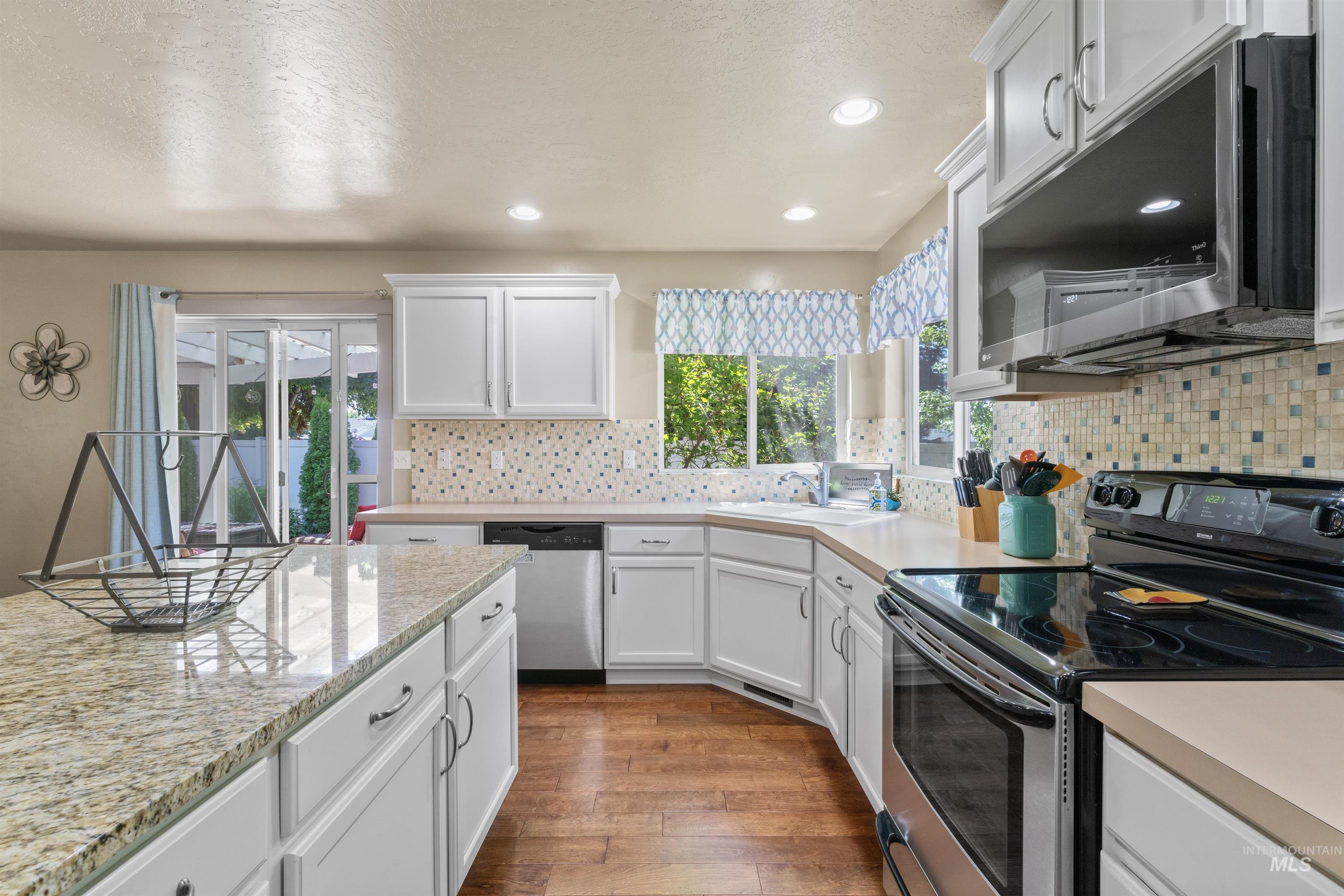 Kitchen featuring appliances with stainless steel finishes, dark wood finished floors, white cabinetry, backsplash, and recessed lighting