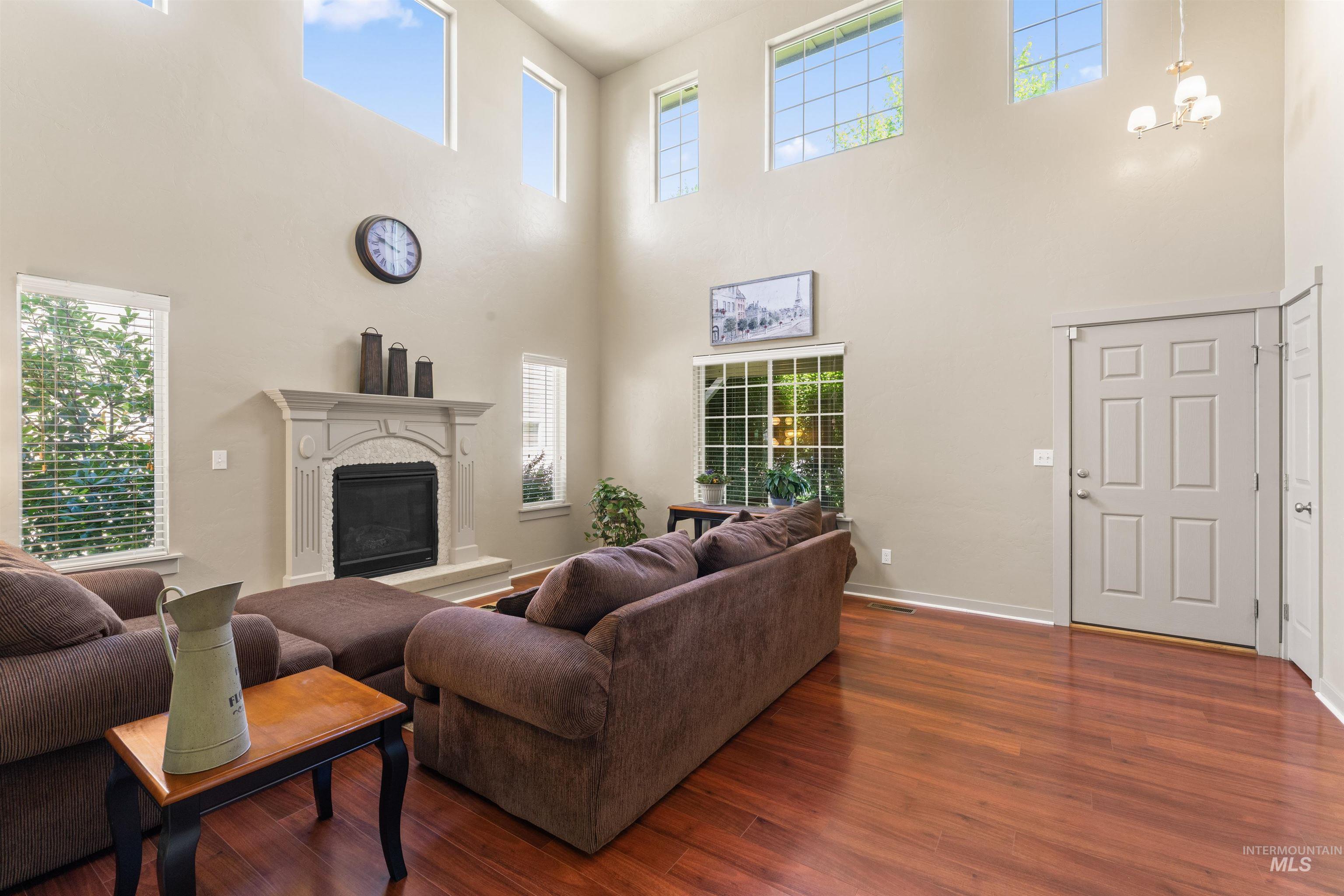 Living area featuring a high ceiling, dark wood-style flooring, plenty of natural light, a high end fireplace, and a chandelier