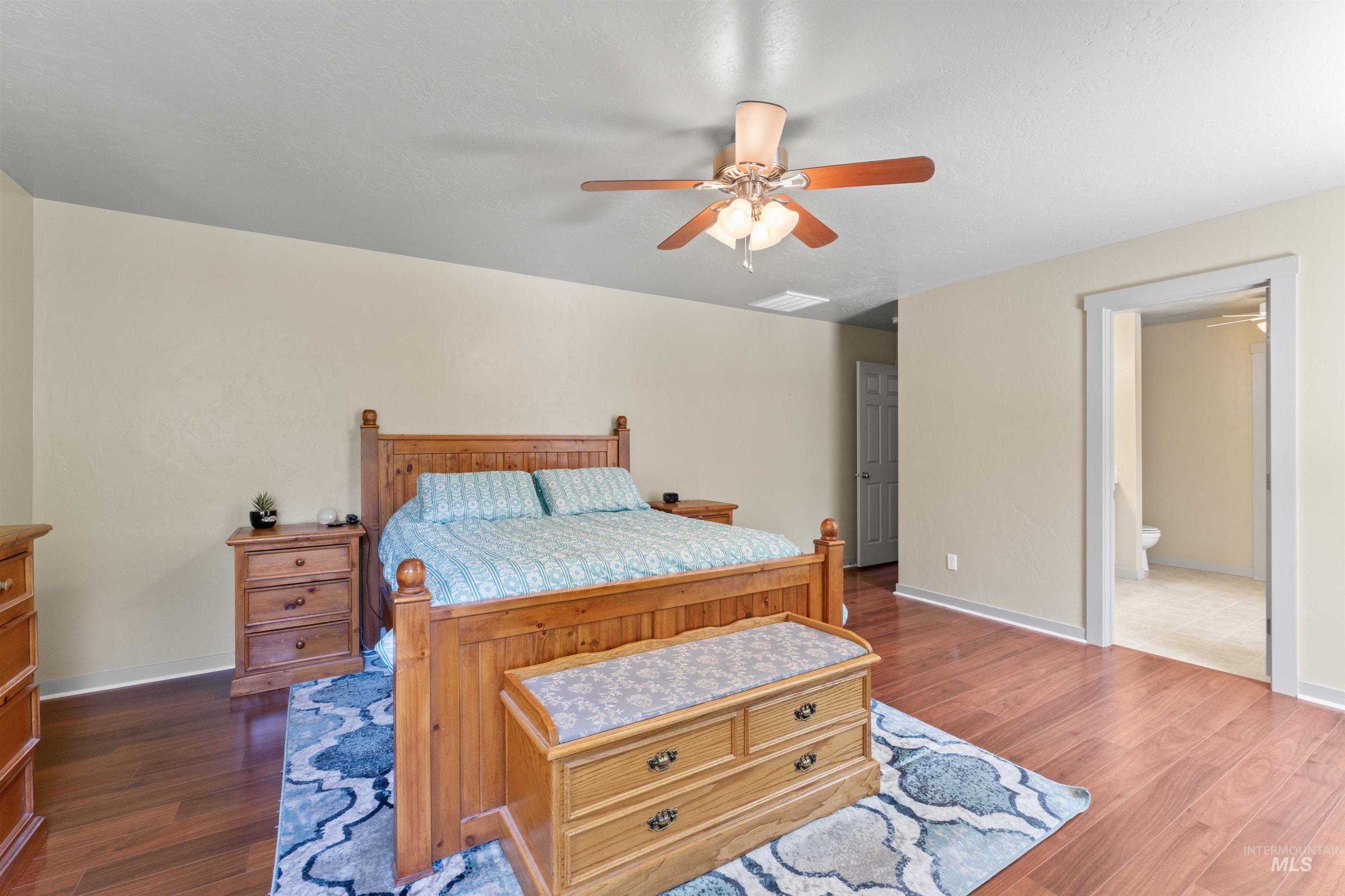 Bedroom with dark wood-type flooring, a ceiling fan, and connected bathroom