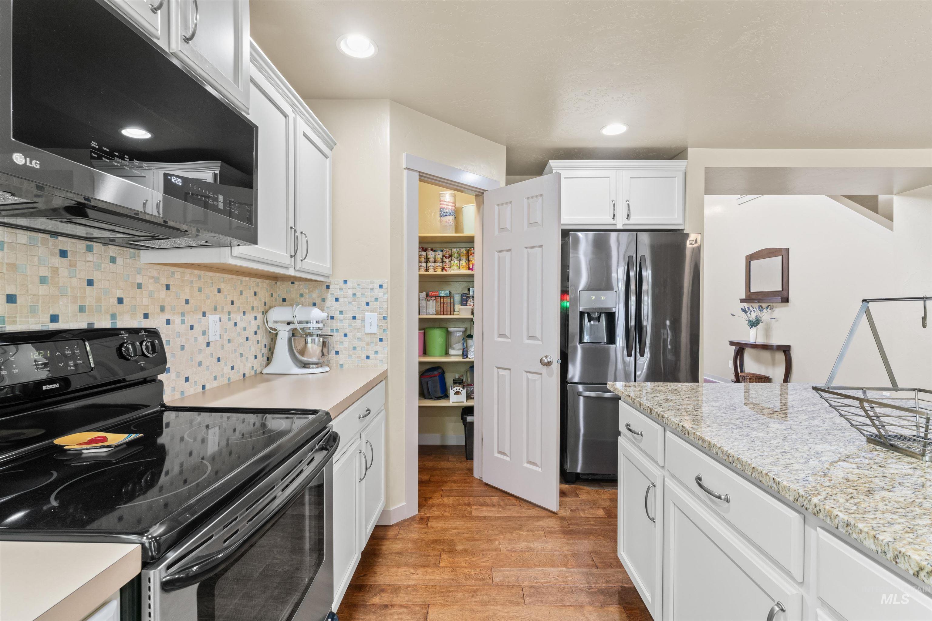 Kitchen with appliances with stainless steel finishes, light wood-style floors, white cabinetry, backsplash, and recessed lighting