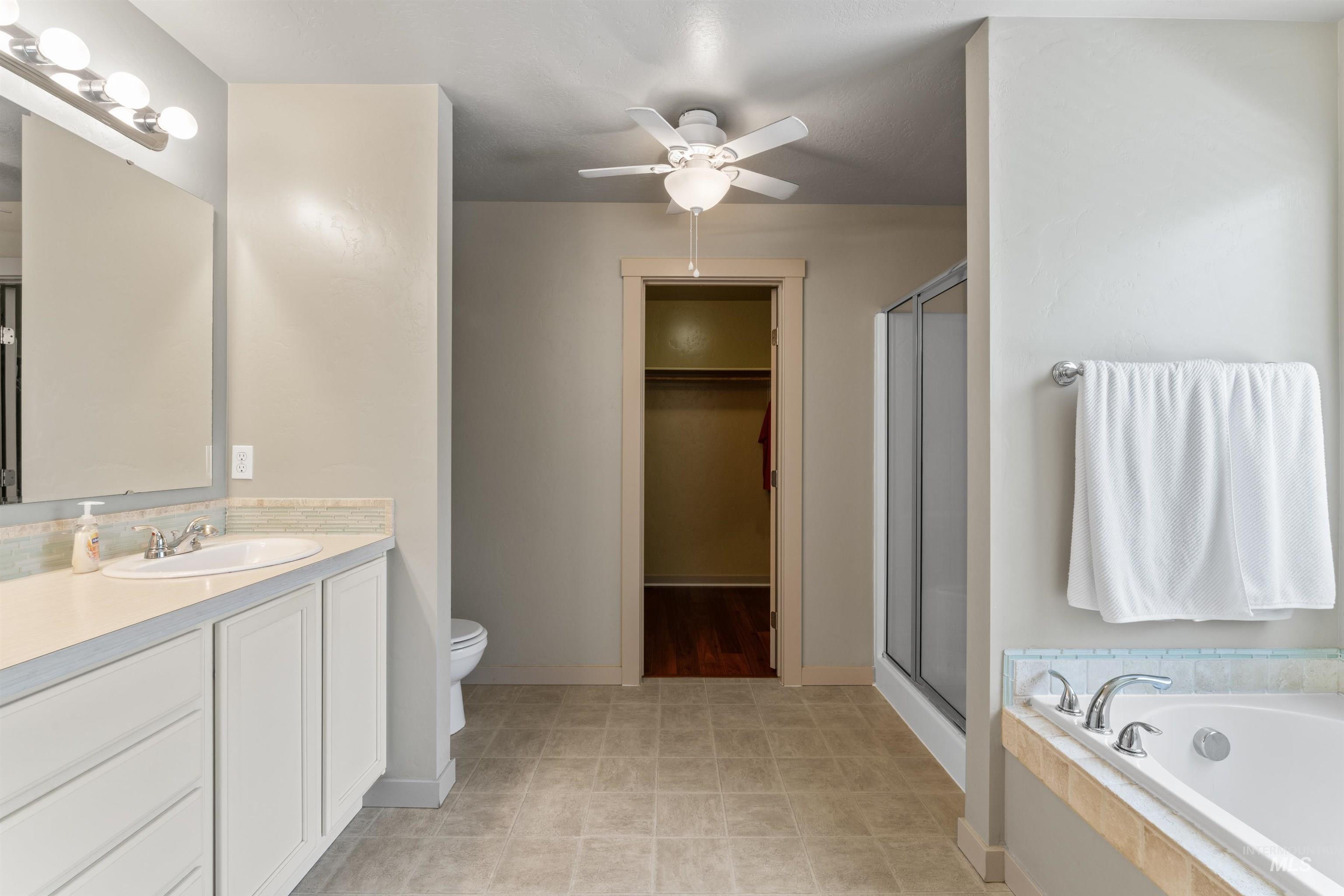 Full bath with vanity, a shower stall, a spacious closet, and a ceiling fan