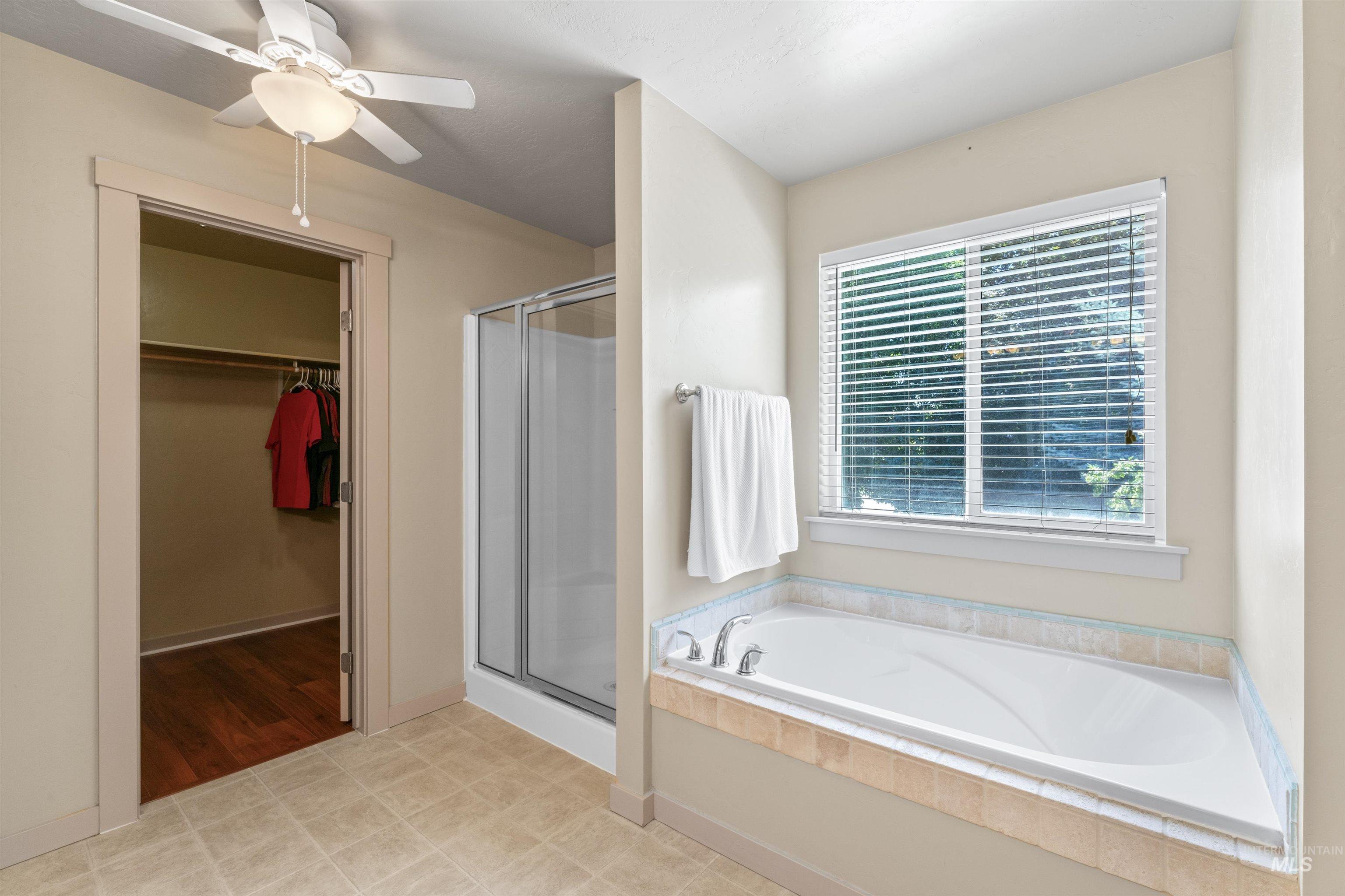 Bathroom with a stall shower, a spacious closet, a bath, and a ceiling fan