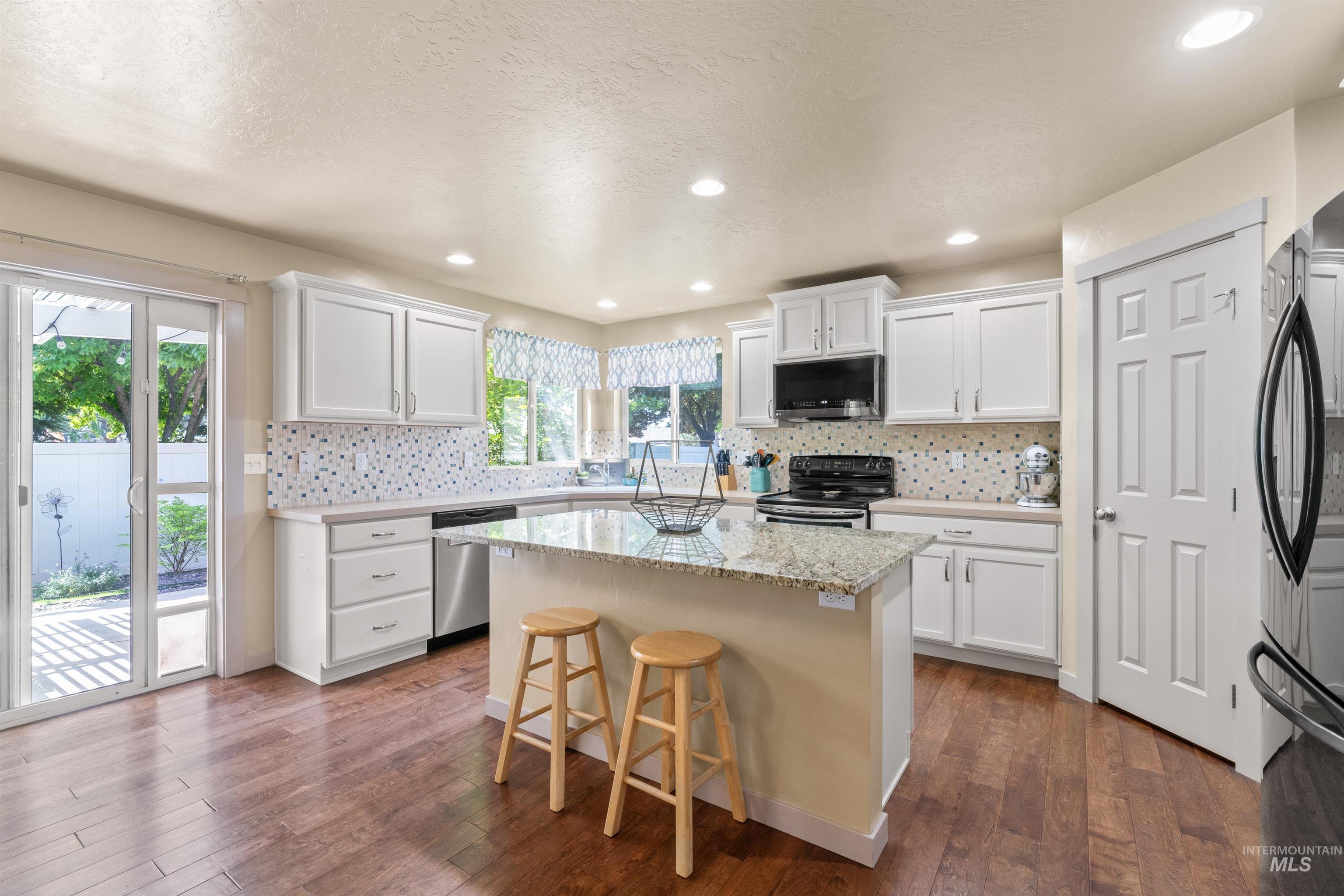 Kitchen with appliances with stainless steel finishes, dark wood-type flooring, a center island, white cabinetry, and a breakfast bar area