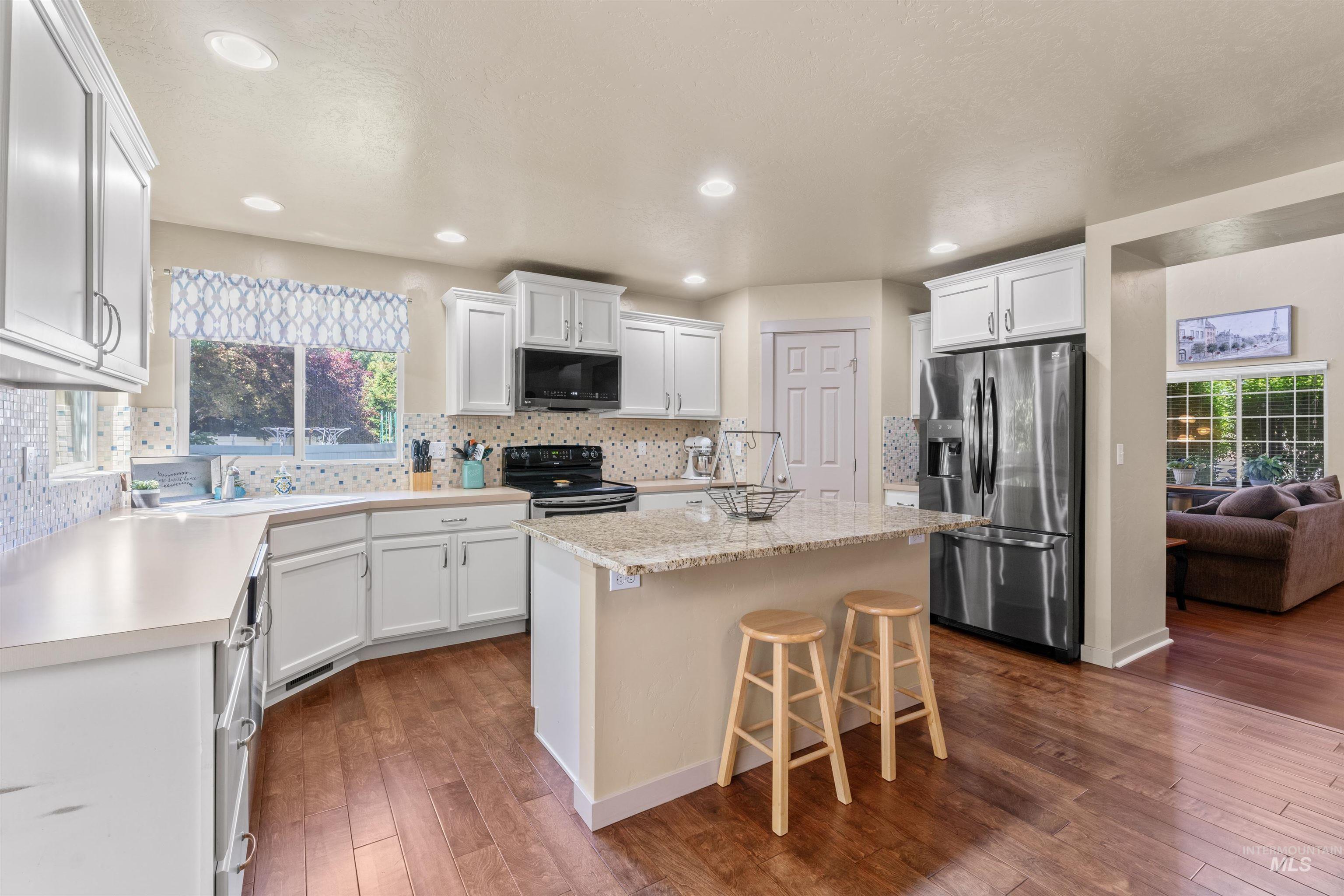 Kitchen featuring stainless steel appliances, a kitchen island, dark wood-style flooring, white cabinets, and recessed lighting