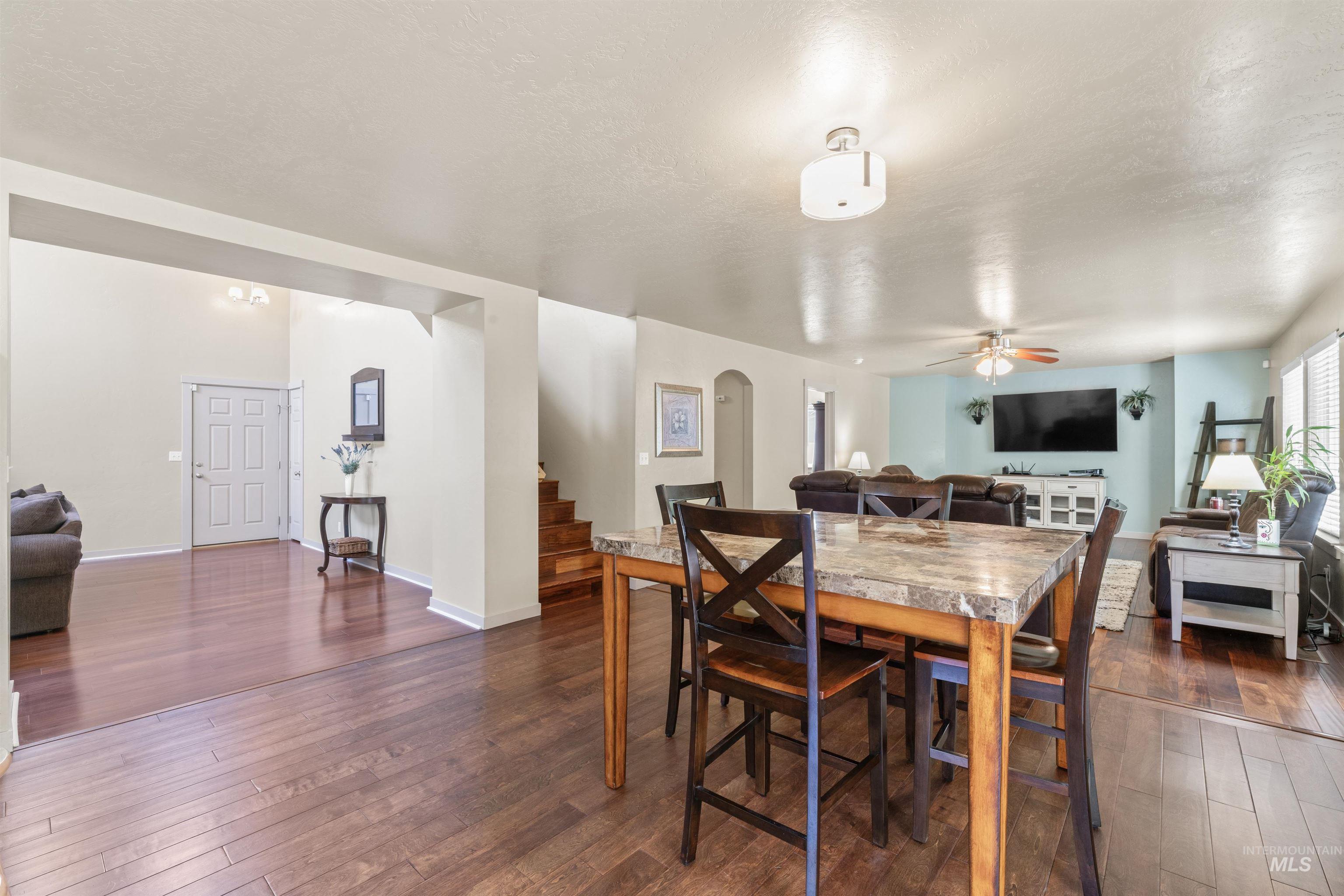 Dining space with a ceiling fan, stairs, dark wood-style flooring, and arched walkways