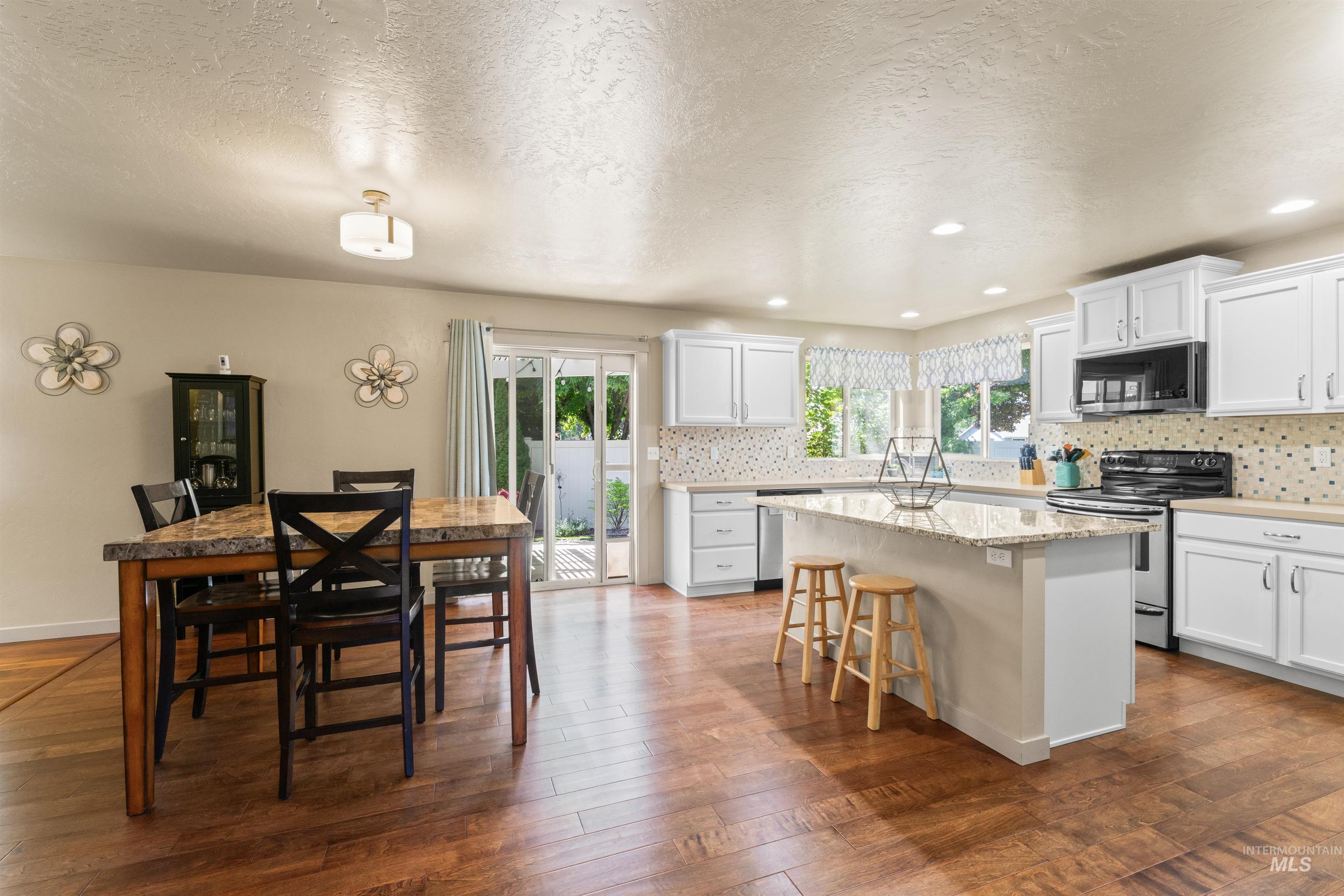 Kitchen featuring stainless steel appliances, a kitchen island, a breakfast bar area, backsplash, and a textured ceiling