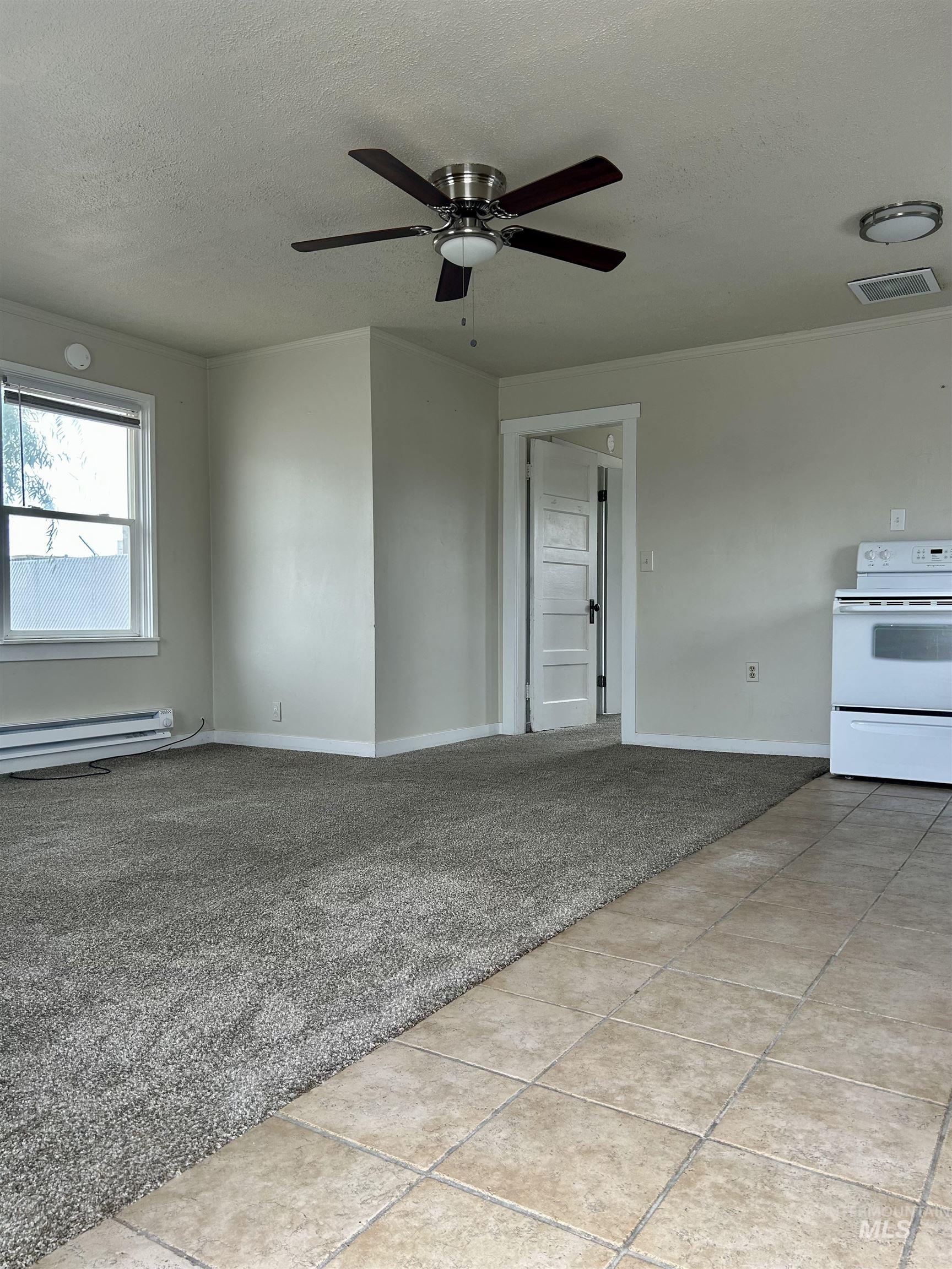 Empty room featuring light carpet, a textured ceiling, light tile patterned floors, a ceiling fan, and a baseboard heating unit