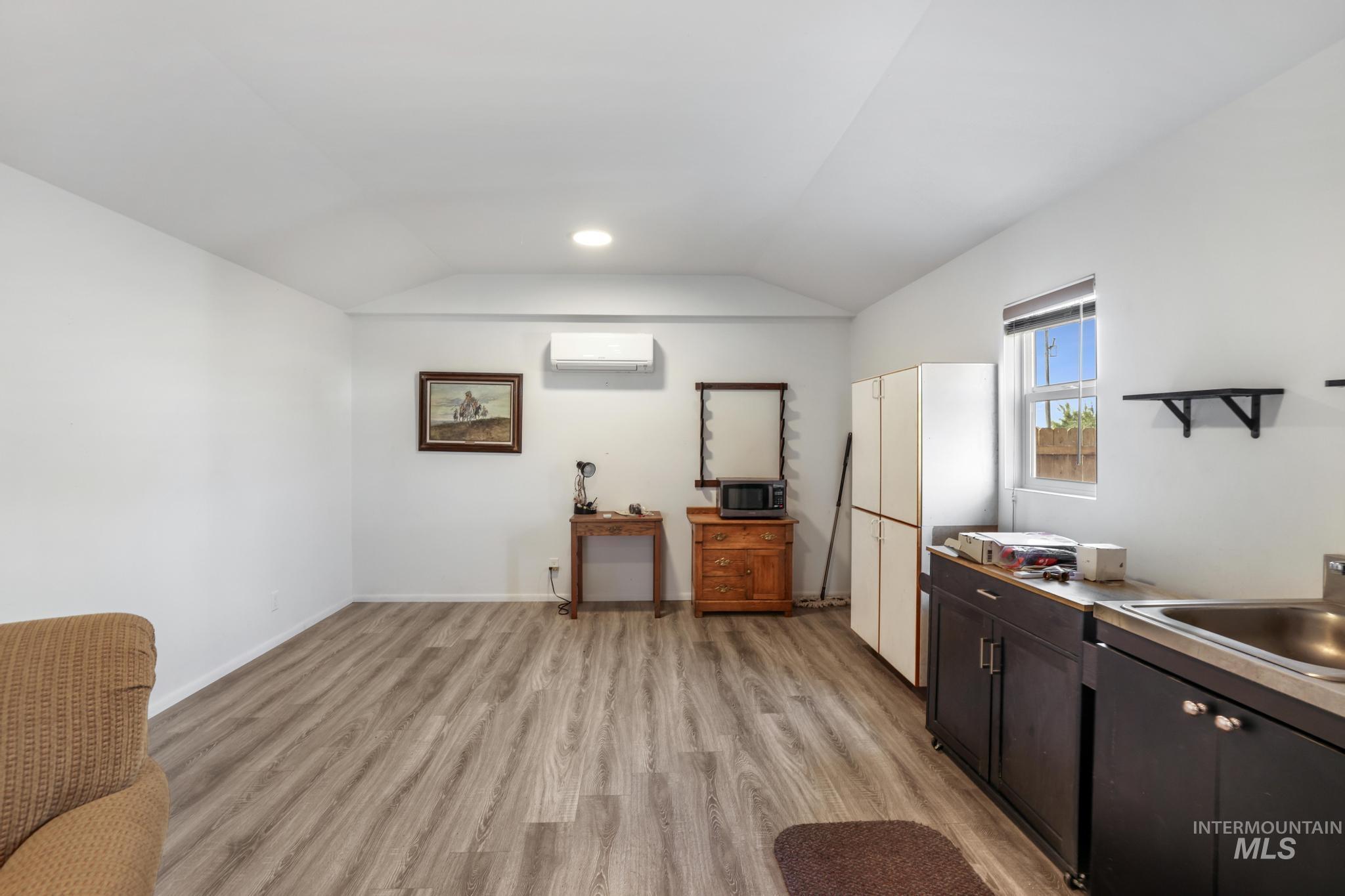 Kitchen with light wood finished floors, vaulted ceiling, dark brown cabinets, stainless steel microwave, and light countertops