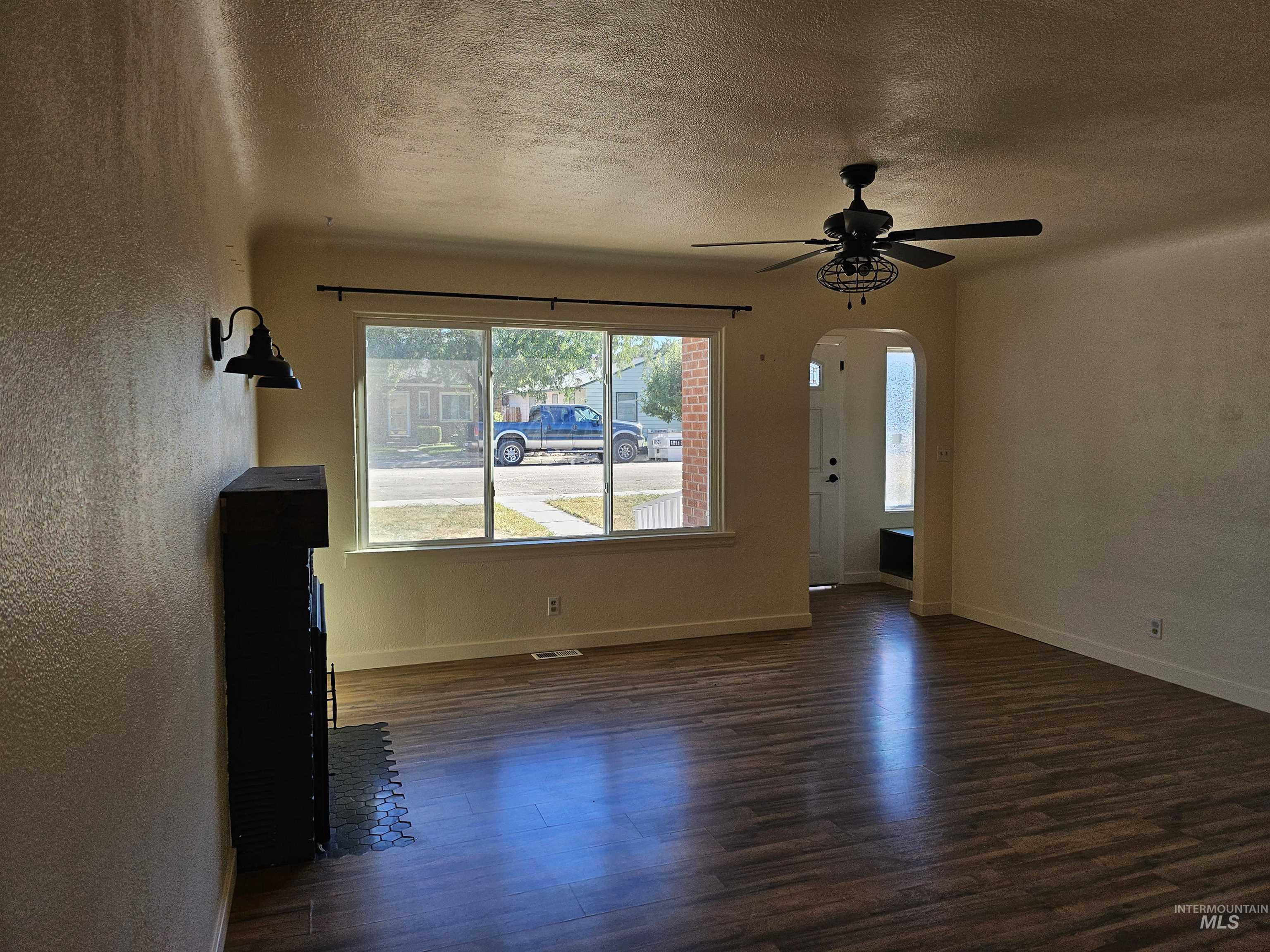 Unfurnished living room featuring a textured ceiling, a textured wall, arched walkways, dark wood finished floors, and ceiling fan