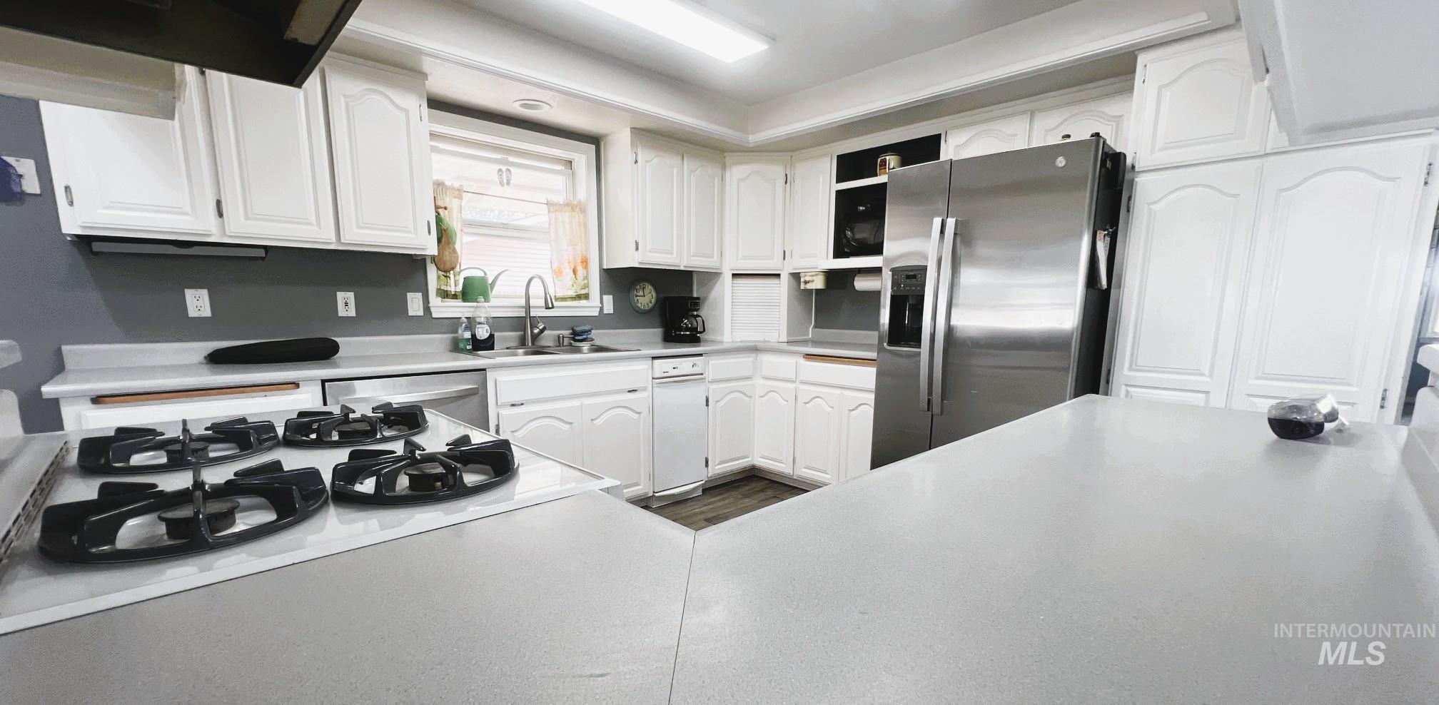 Kitchen with appliances with stainless steel finishes, white cabinetry, light countertops, and exhaust hood