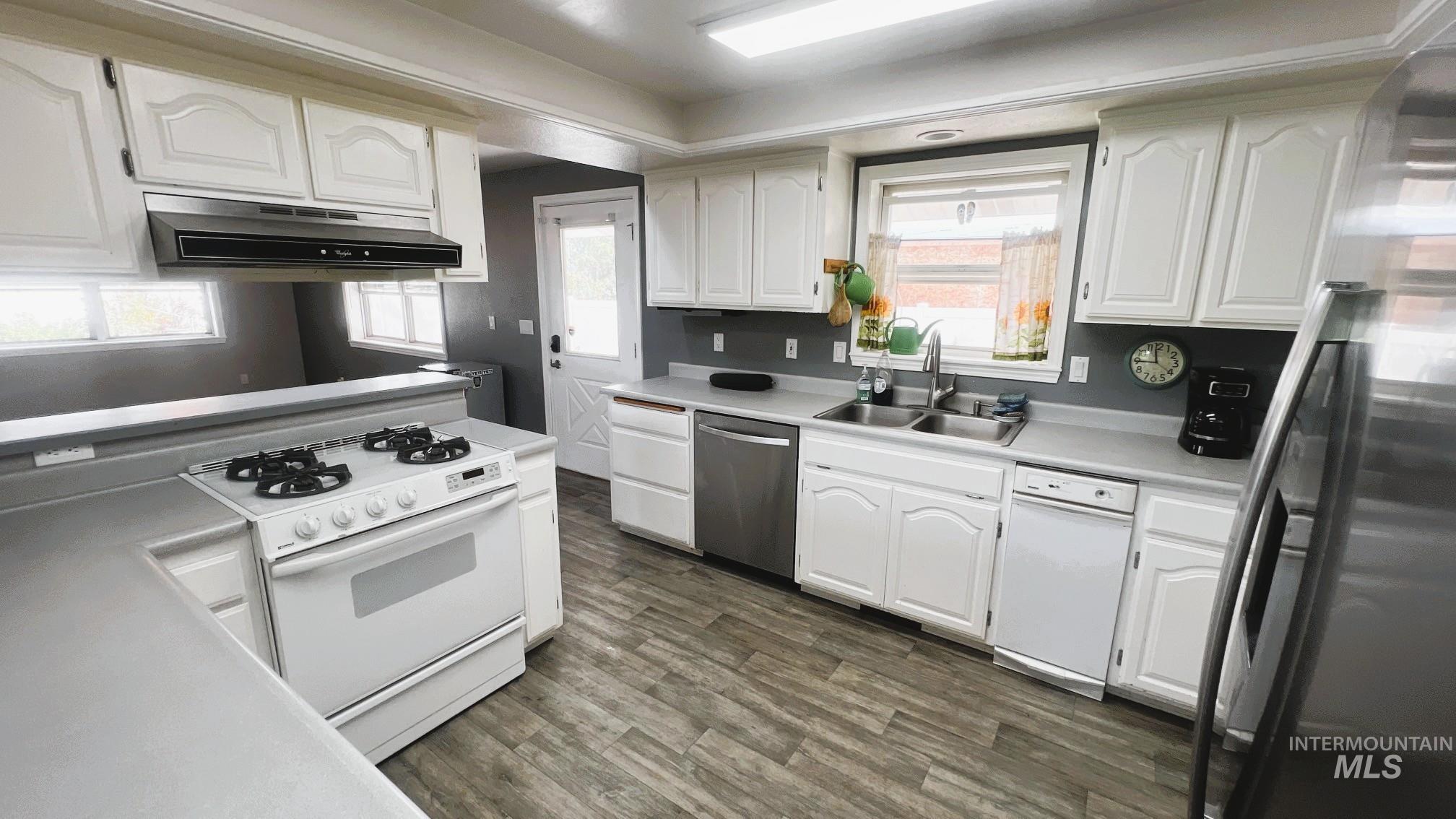 Kitchen with stainless steel appliances, white cabinetry, dark wood-style floors, light countertops, and under cabinet range hood