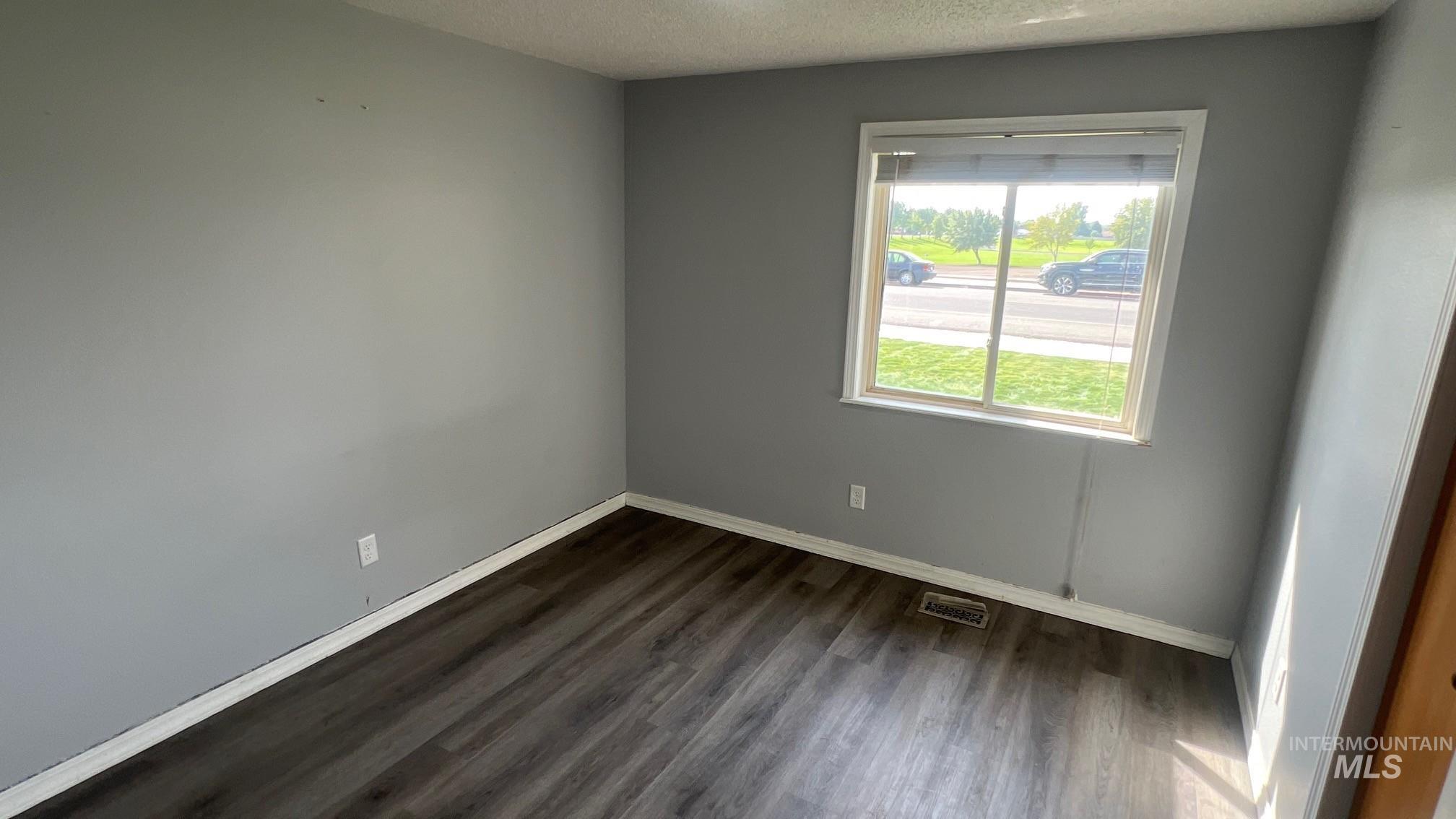 Empty room featuring dark wood-type flooring and a textured ceiling