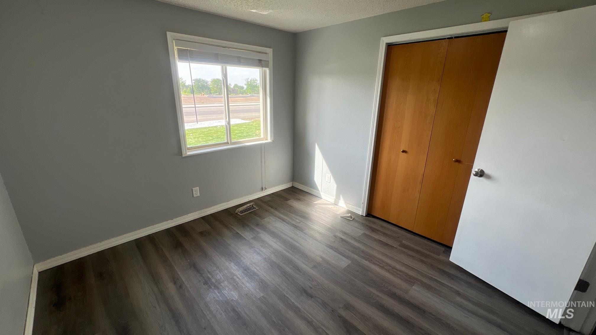 Unfurnished bedroom featuring a textured ceiling, dark wood-style floors, and a closet