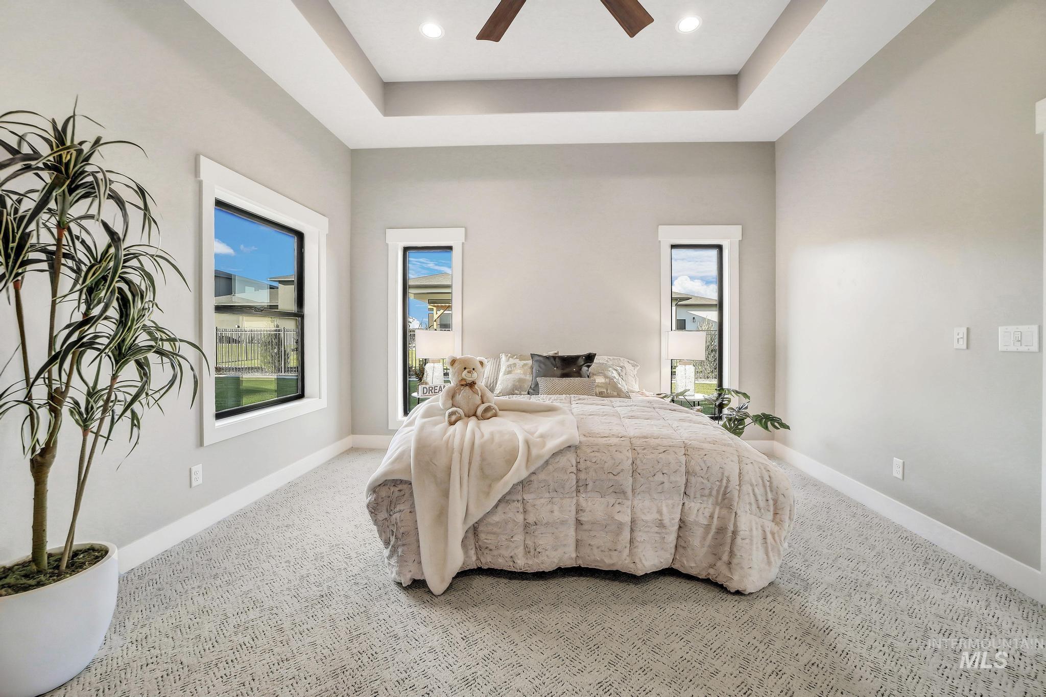 Carpeted bedroom featuring a raised ceiling, ceiling fan, and recessed lighting
