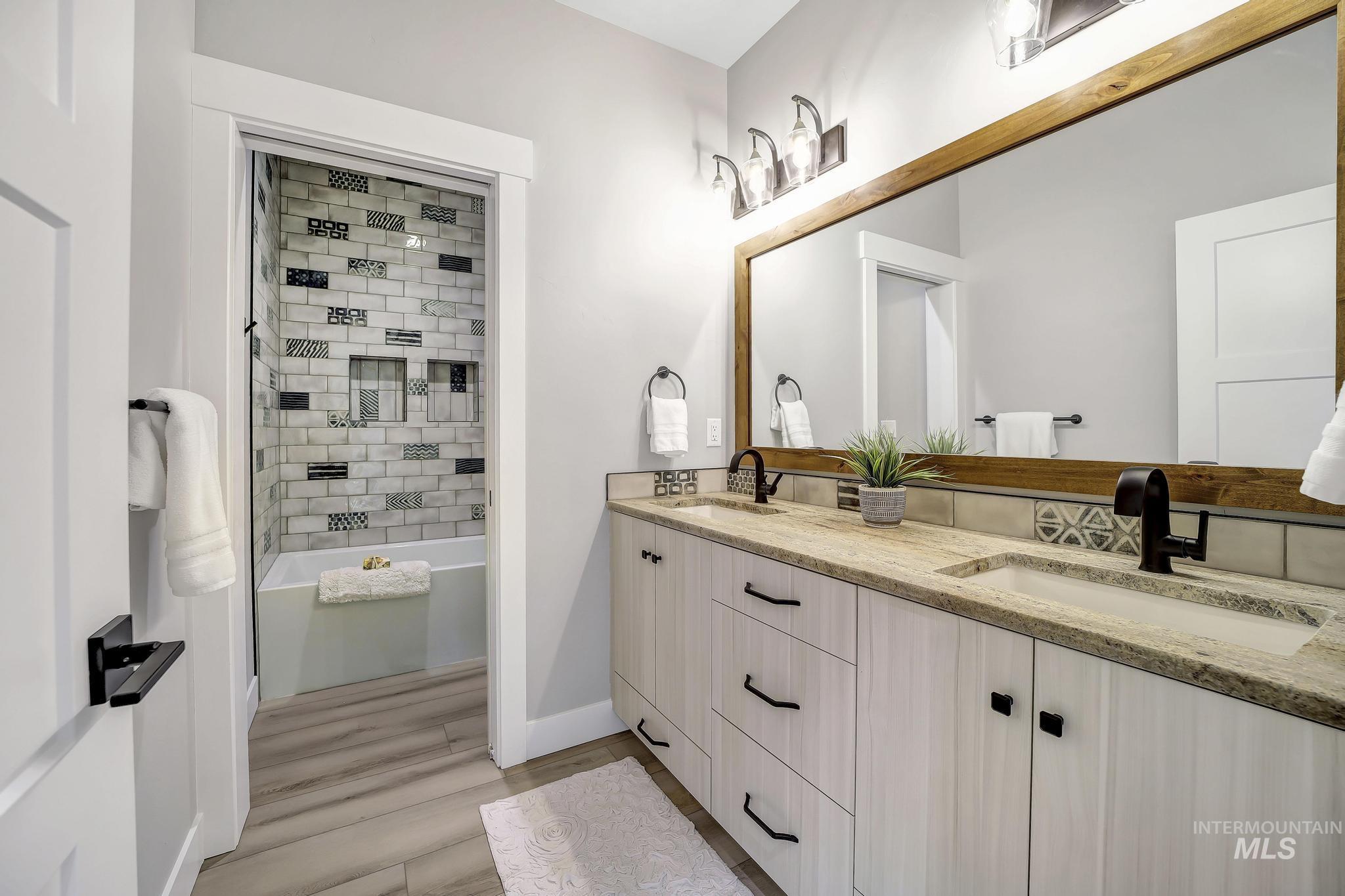 Bathroom with shower / tub combination, double vanity, and light wood-type flooring