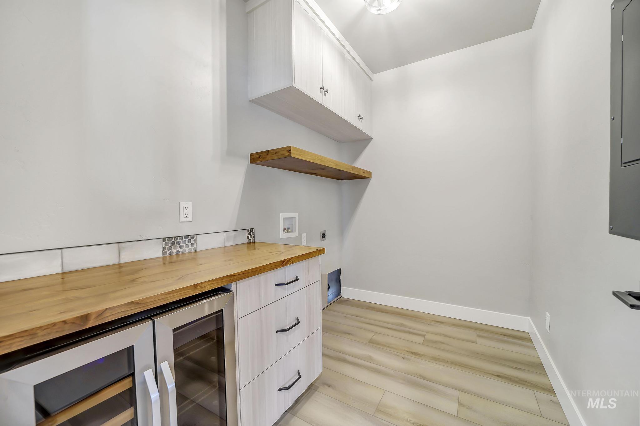 Bar featuring wooden counters, wine cooler, open shelves, white cabinetry, and electric panel