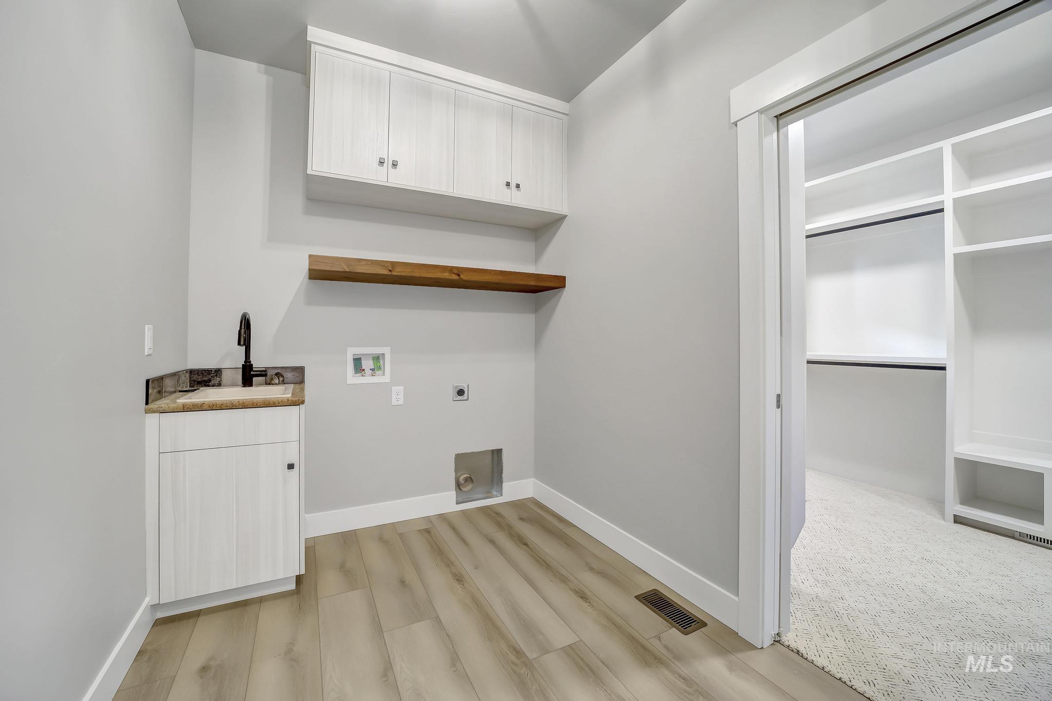Washroom featuring hookup for an electric dryer, light wood-type flooring, washer hookup, cabinet space, and bar with sink