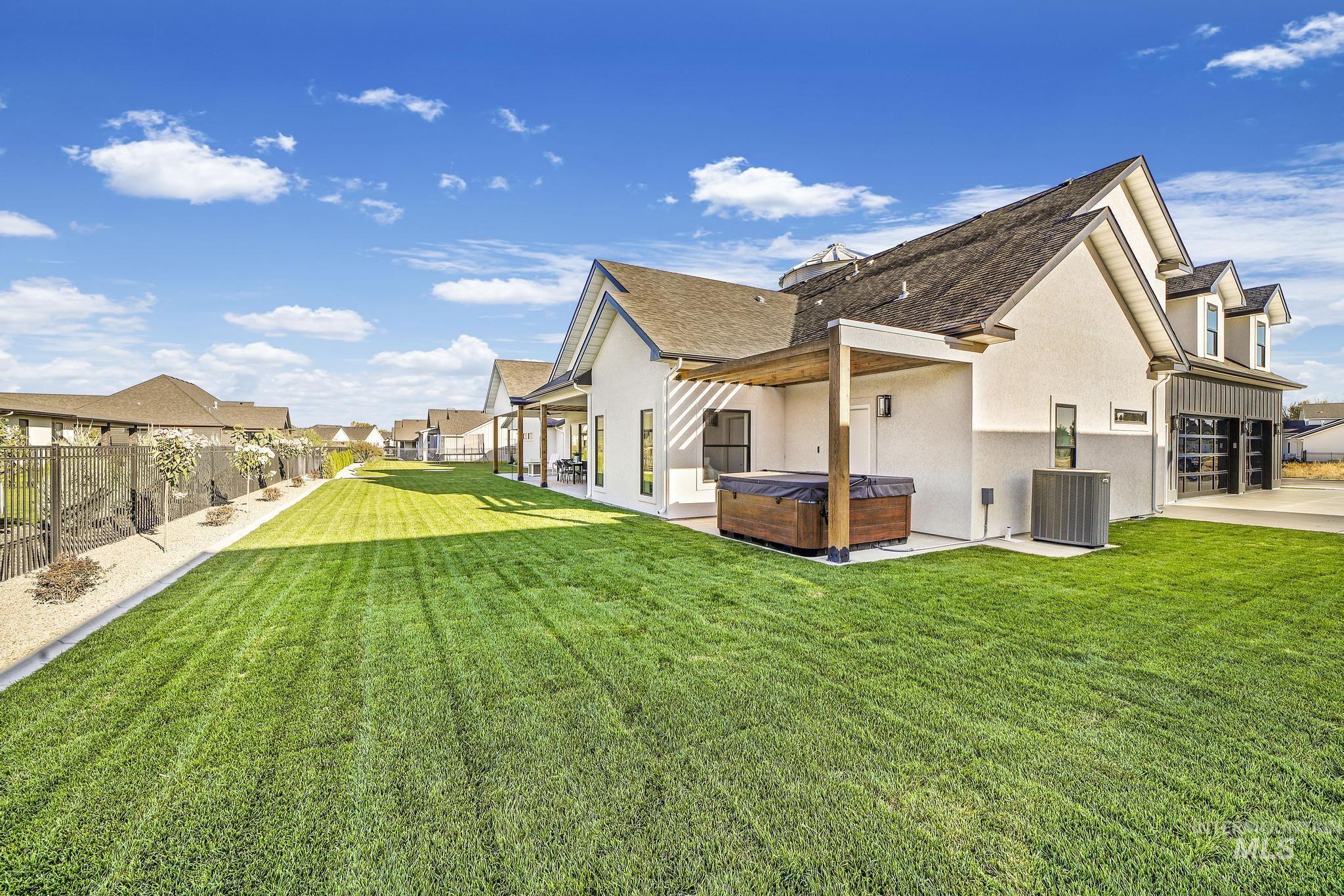 Back of house with a hot tub, stucco siding, a patio area, a fenced backyard, and roof with shingles